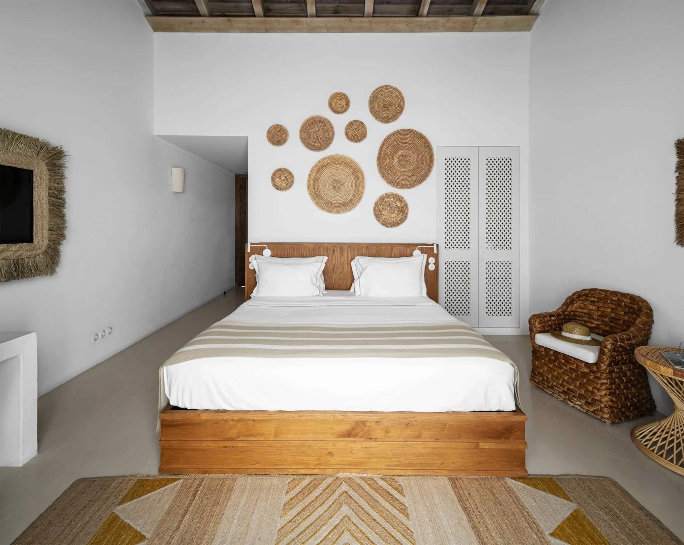 Doppelbett aus Holz mit weißer Bettwäsche und runden Wanddekorationen aus Naturfasern darüber.