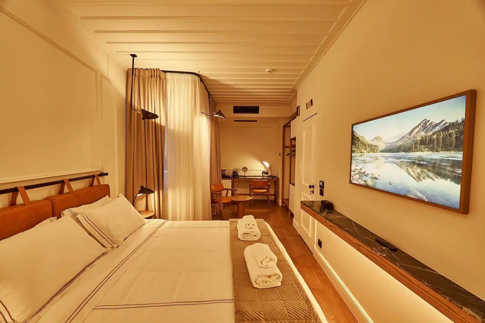 Hotelzimmer mit Doppelbett, Fernseher an der Wand und Schreibtisch im Hintergrund.
