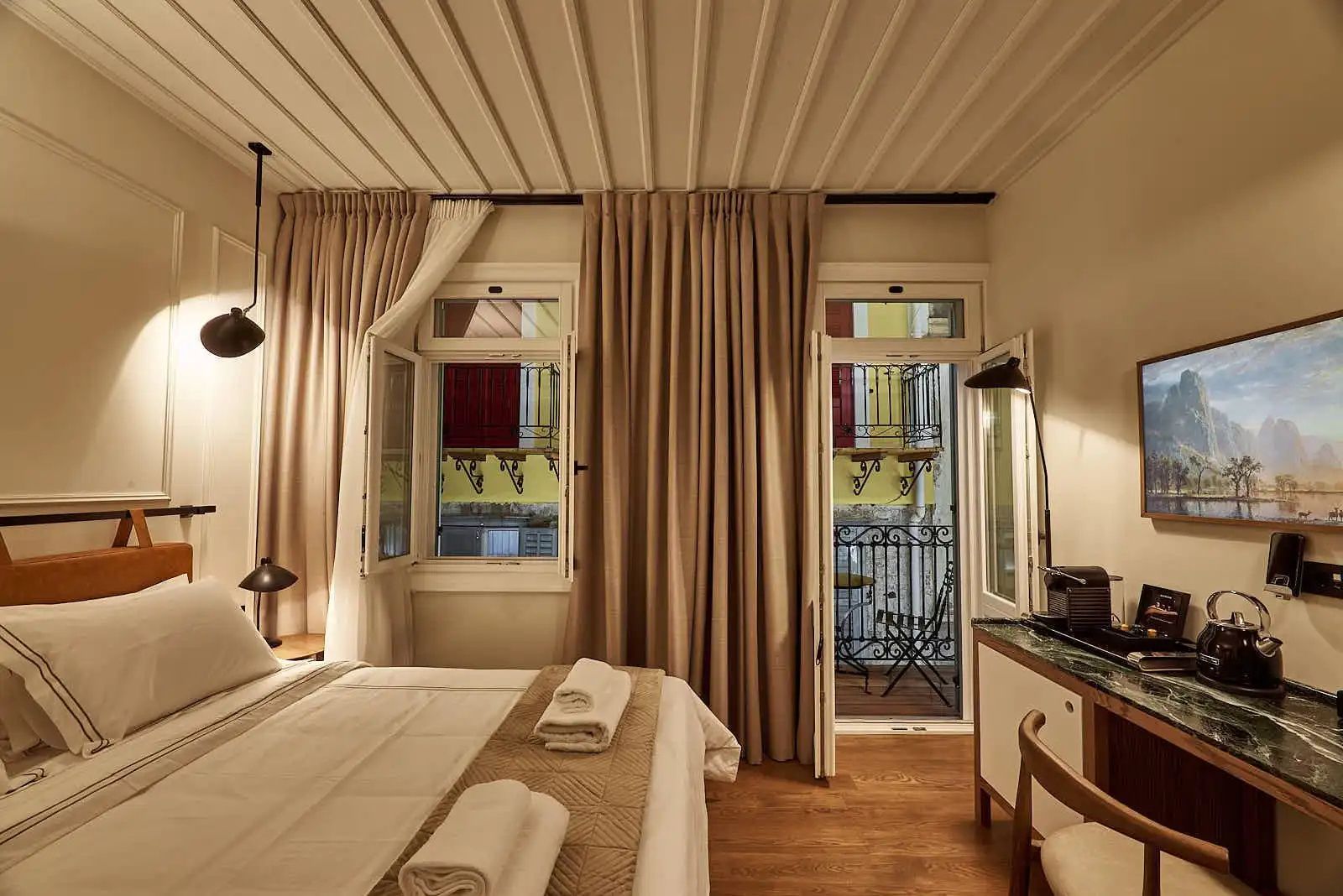 Fenster und geöffnete Balkontür in einem hellen Hotelzimmer mit Holzfußboden.