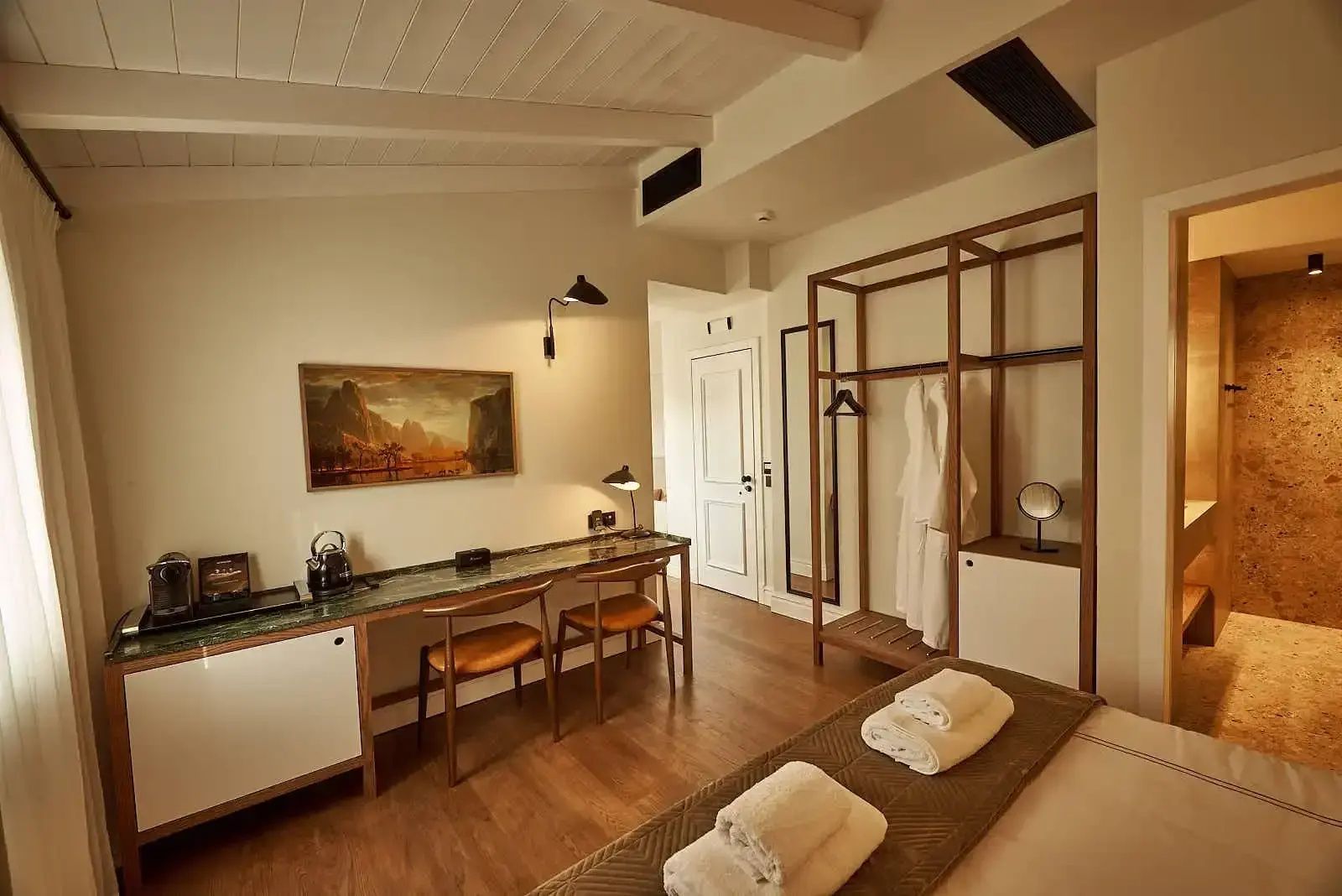 Hotelzimmer mit langem Schreibtisch, Holzstühlen, Kunstwerk an der Wand und offenem Kleiderschrank