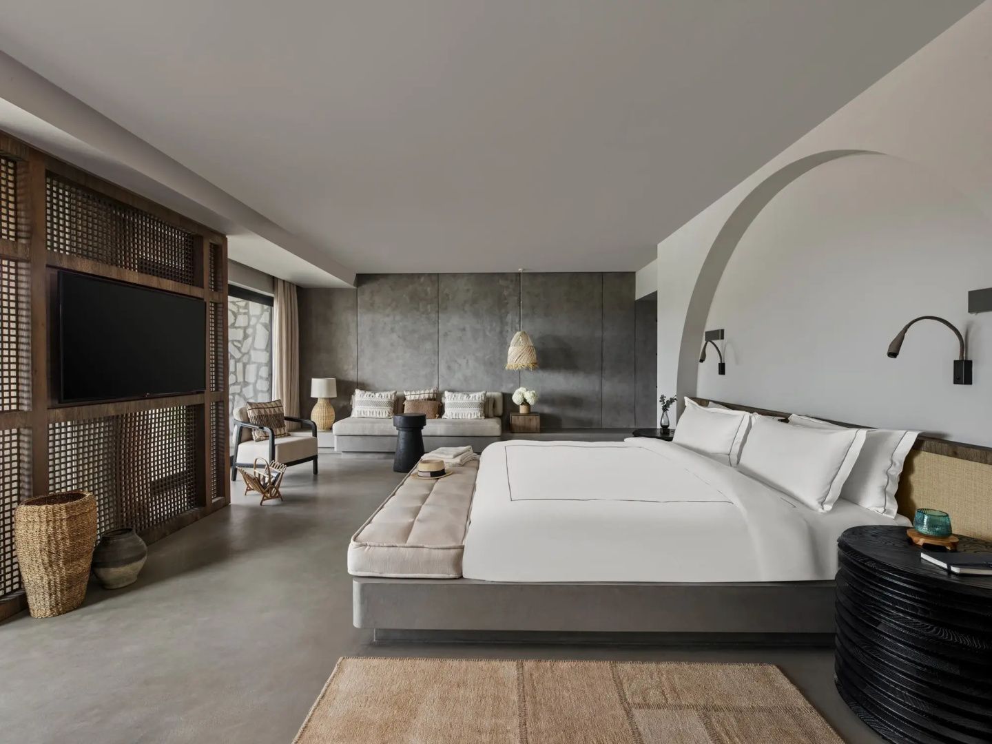 Modernes Hotelzimmer mit Doppelbett, Sitzbereich, Couch und einem Fernseher an der Wand.