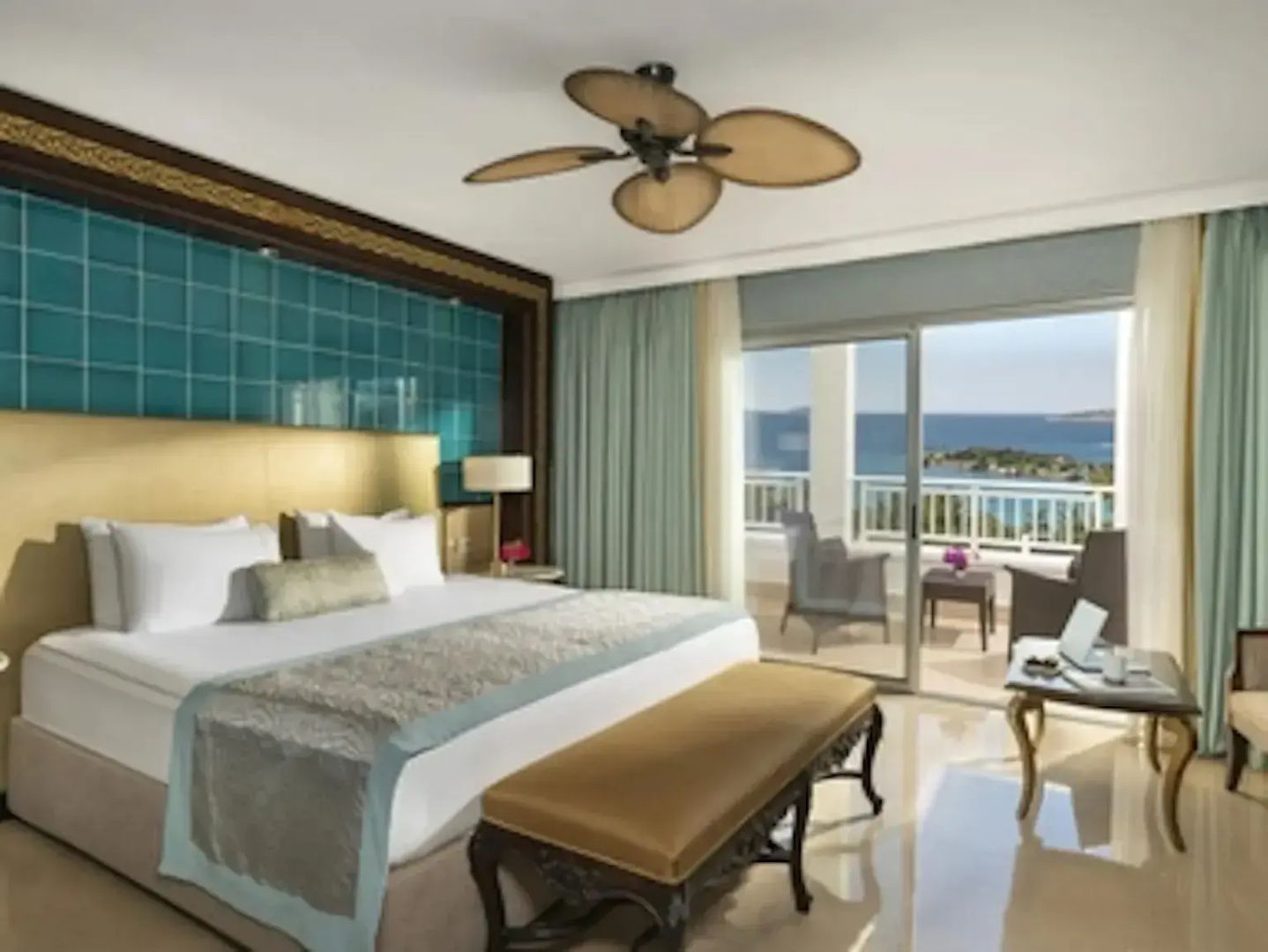 Helles Hotelzimmer mit Doppelbett, Deckenventilator und Balkon mit direktem Blick auf das Meer.