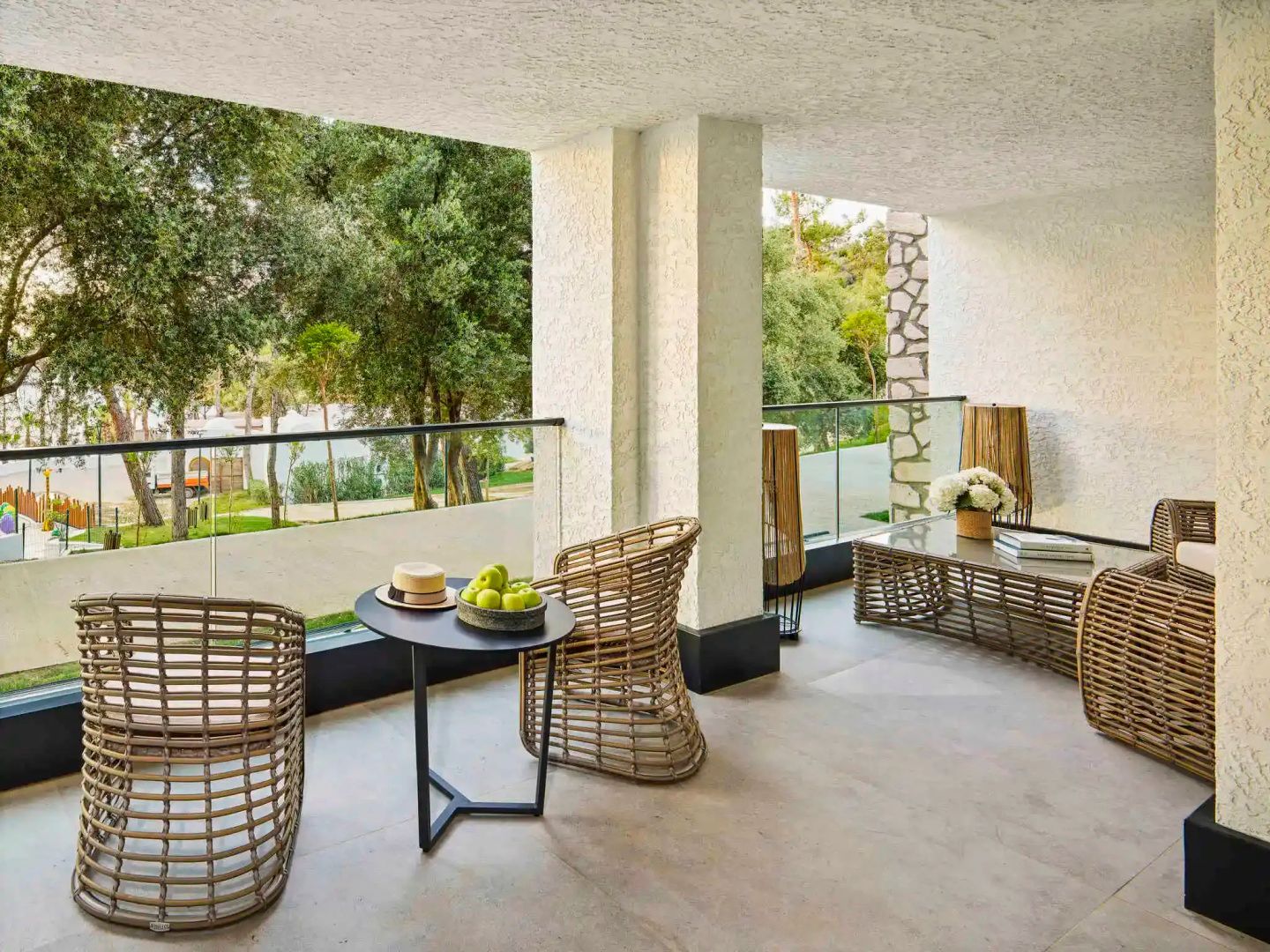 Überdachte Terrasse mit Sitzgelegenheiten aus Geflecht und Blick auf Bäume im Außenbereich.