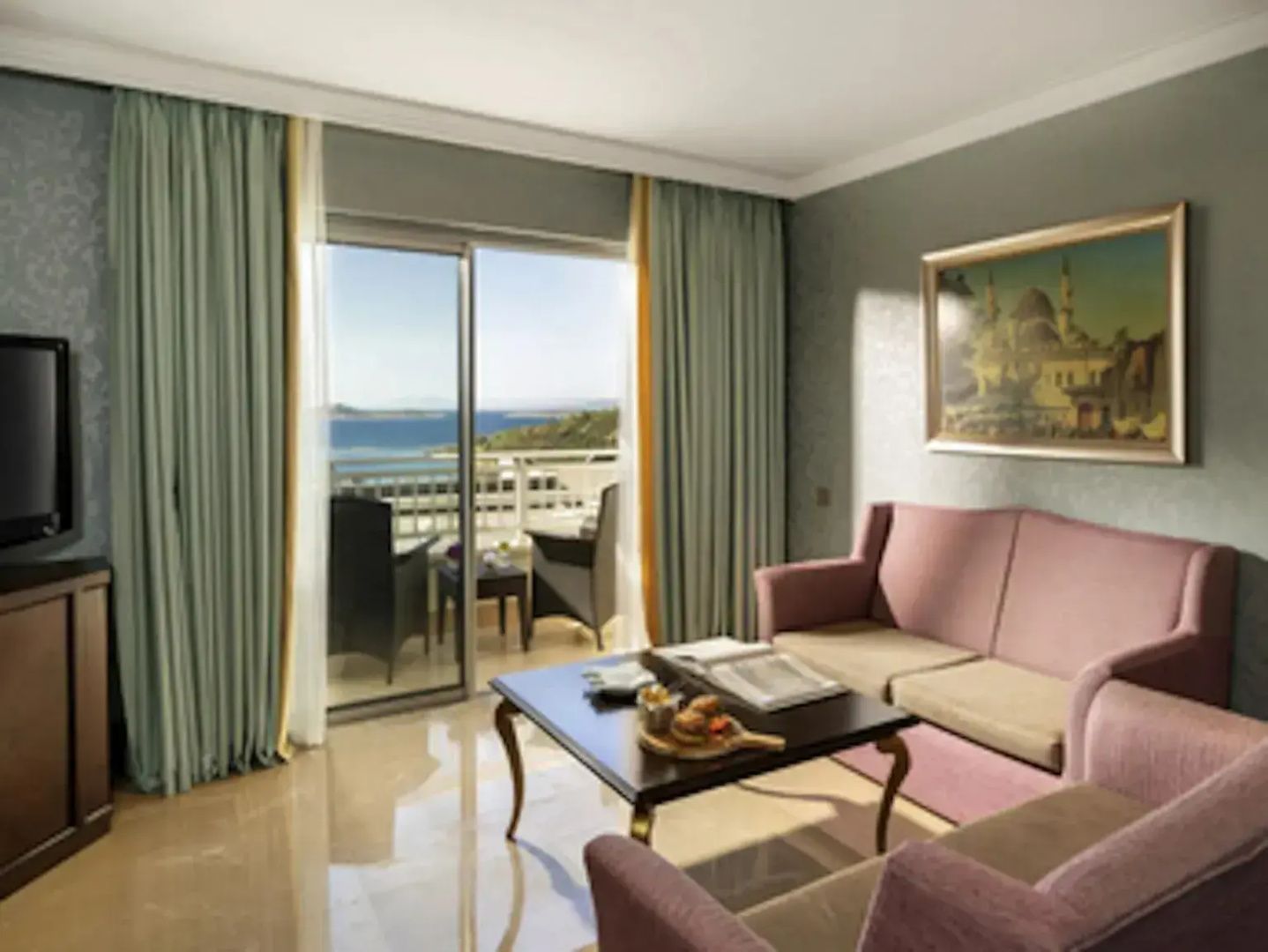 Wohnbereich mit rosa Sofas, Couchtisch und Blick durch die Balkontür auf das Meer.