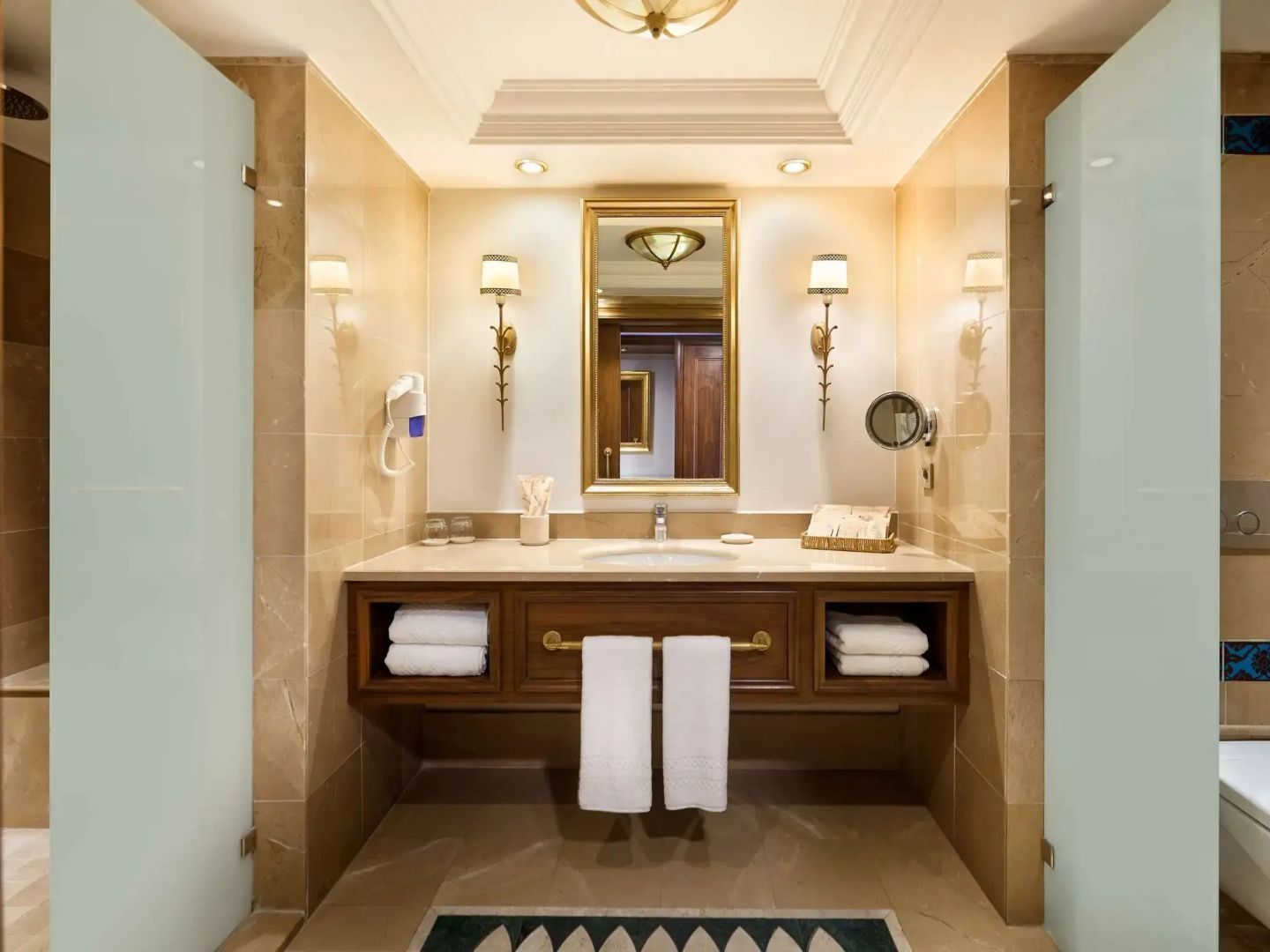 Badezimmer mit hölzernem Waschtisch, großem Spiegel, Wandleuchten und Handtüchern.