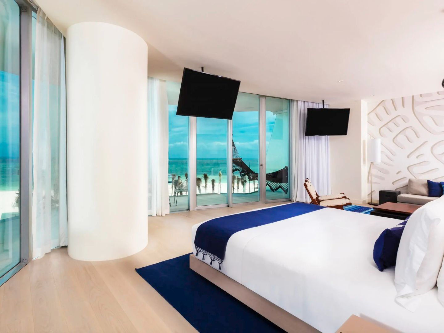 Modernes Hotelzimmer mit Doppelbett, blauen Akzenten und bodentiefen Fenstern zum Meer.