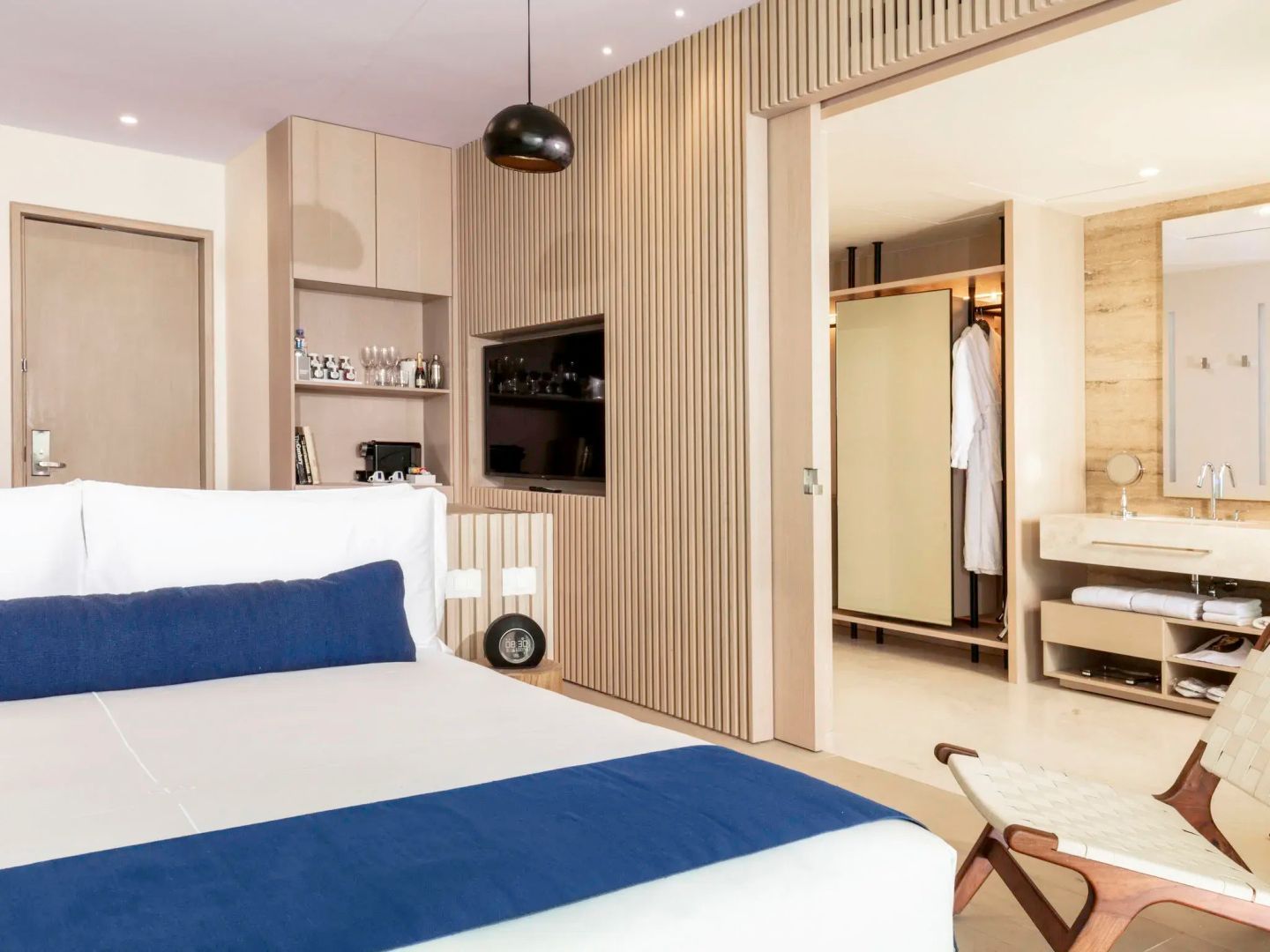 Modernes Hotelzimmer mit Bett, Holzlamellenwand, Flachbild-TV und Durchgang zum Ankleidebereich.