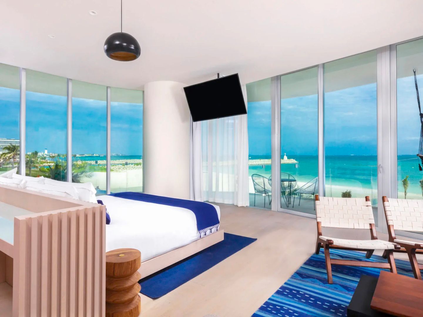Helles Schlafzimmer mit Doppelbett, Sessel und Blick durch Panoramafenster auf das Meer.
