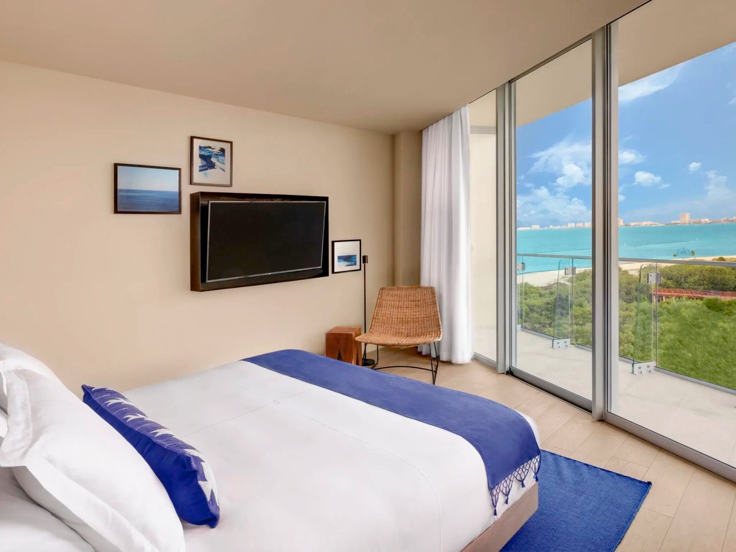 Schlafbereich mit Doppelbett, Fernseher an der Wand und Fenstertür zum Balkon mit Meerblick