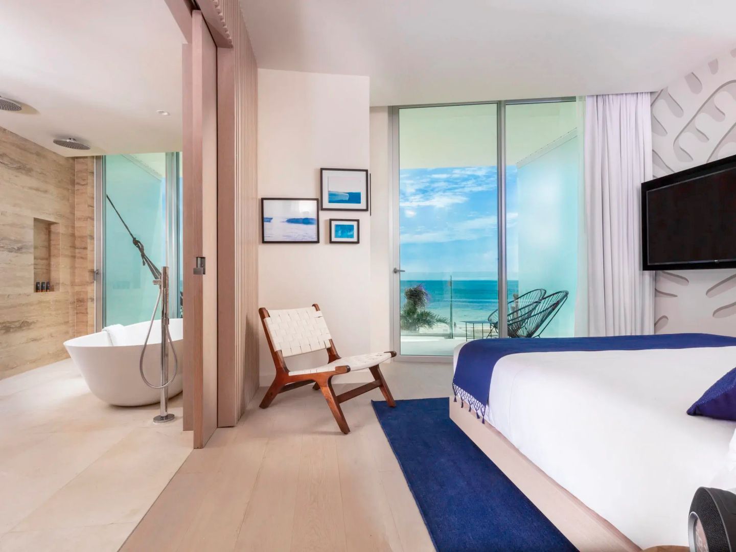 Helles Hotelzimmer mit Doppelbett, Stuhl, Badzugang und Blick durch das Fenster auf das Meer.
