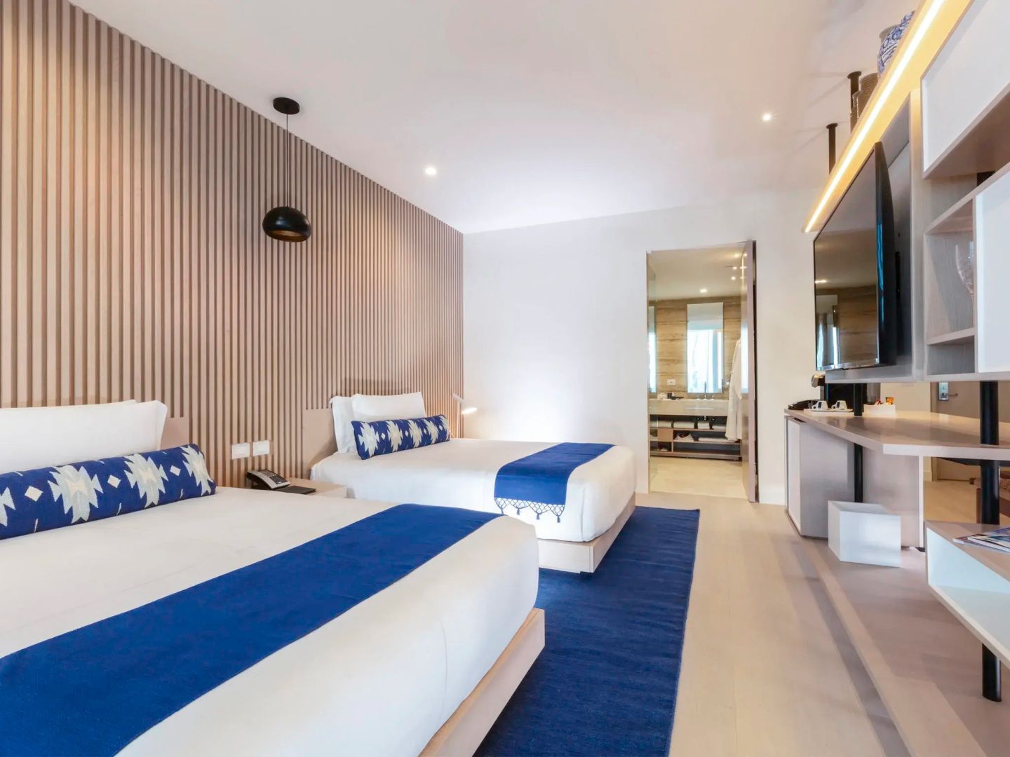 Modernes Doppelzimmer mit zwei Betten, holzverkleideter Wand und Durchgang zum Badezimmer.