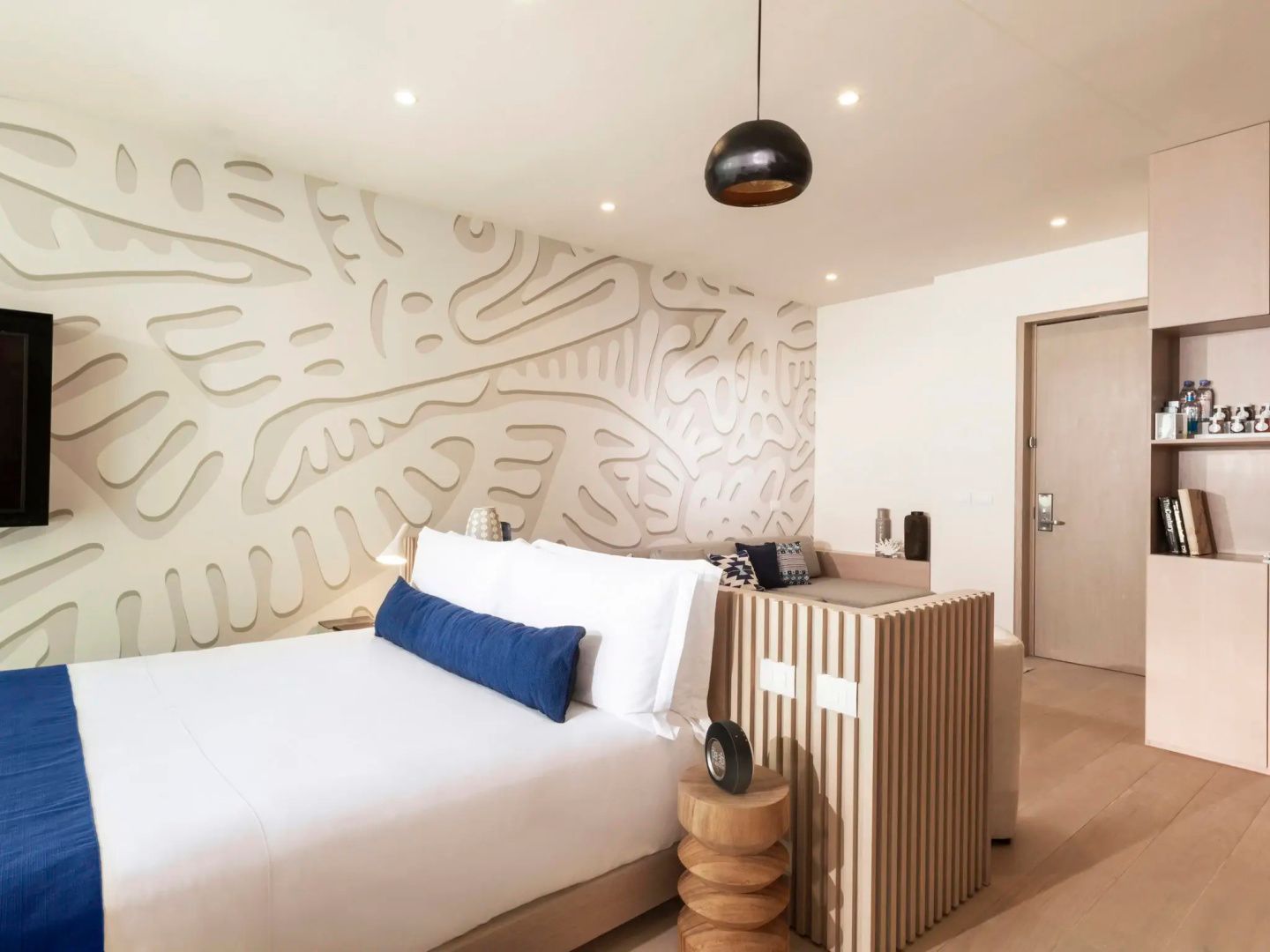 Doppelbett mit weißer Bettwäsche und kunstvoll strukturierter Wandgestaltung dahinter