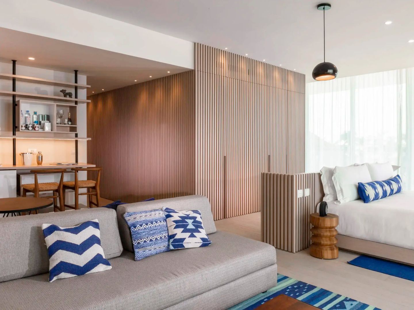 Wohnbereich einer Suite mit grauem Sofa, blauen Kissen und hellen Holzverkleidungen.