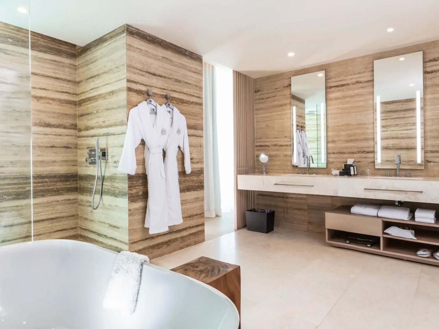 Badezimmer mit Natursteinwänden, freistehender Badewanne und Doppelwaschtisch.