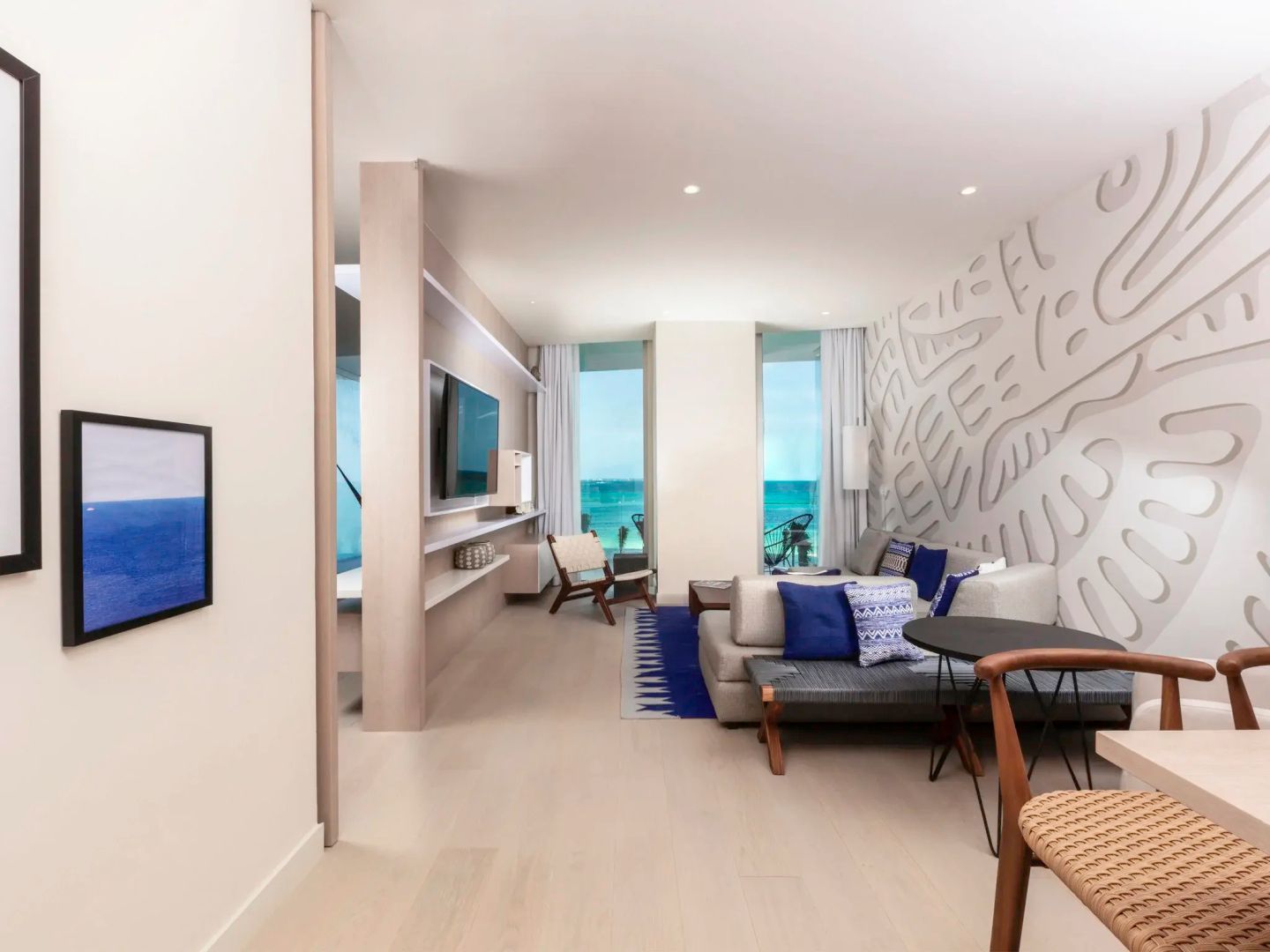 Modern eingerichtetes Suite-Wohnzimmer mit Sofa, Holzboden und Fensterfront zum Meer.