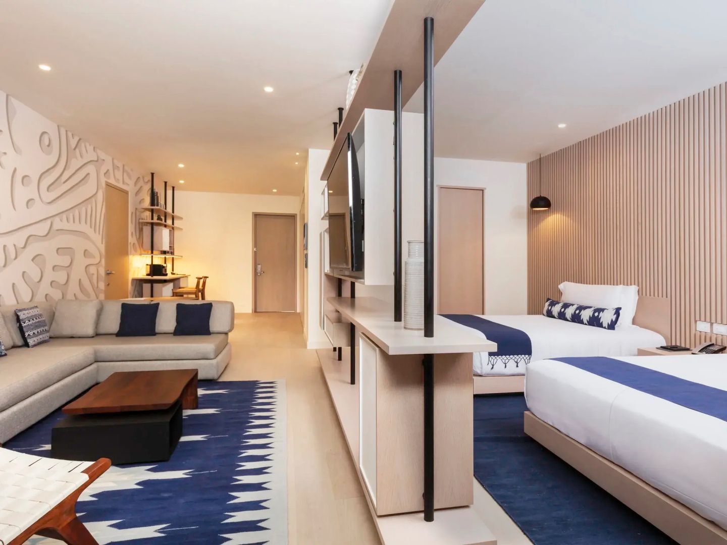 Großes Hotelzimmer mit Sofaecke, Couchtisch und zwei Betten, getrennt durch Raumteiler