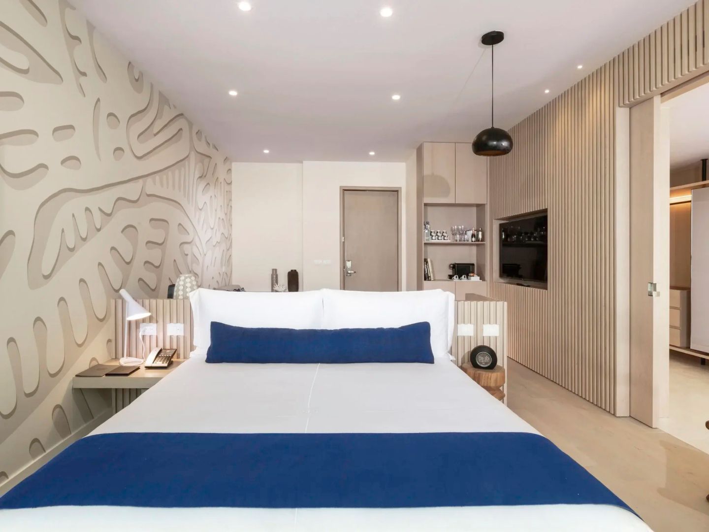 Blick auf ein Bett mit blauer Tagesdecke und helle Holzverkleidung an den Wänden im Zimmer