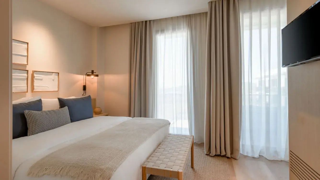 Helles Schlafzimmer mit Doppelbett, Sitzbank und bodentiefen Fenstern.