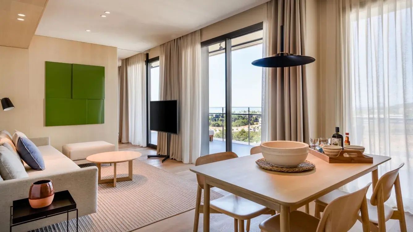 Modernes Wohnzimmer einer Suite mit Esstisch, Fernseher und Balkonzugang.