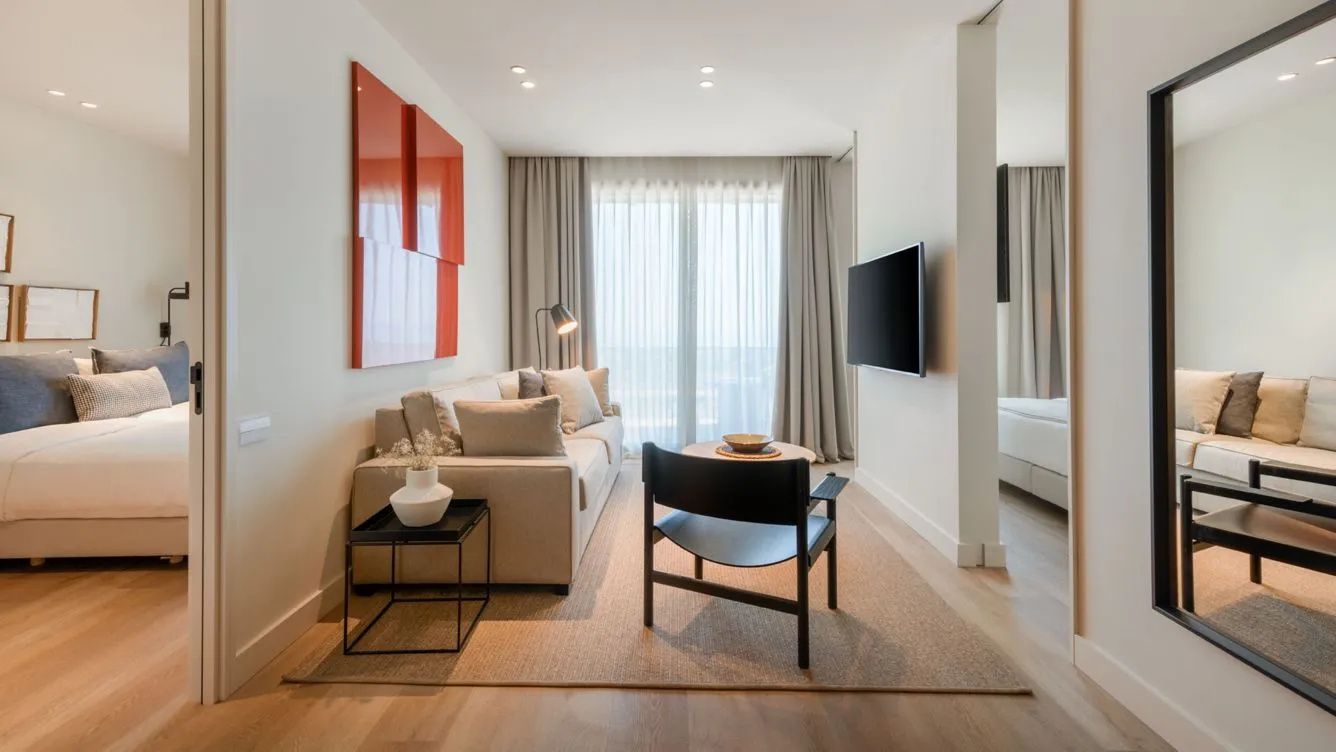 Wohnbereich einer Suite mit hellem Sofa, Sessel, Couchtisch und Flachbild-Fernseher an der Wand.