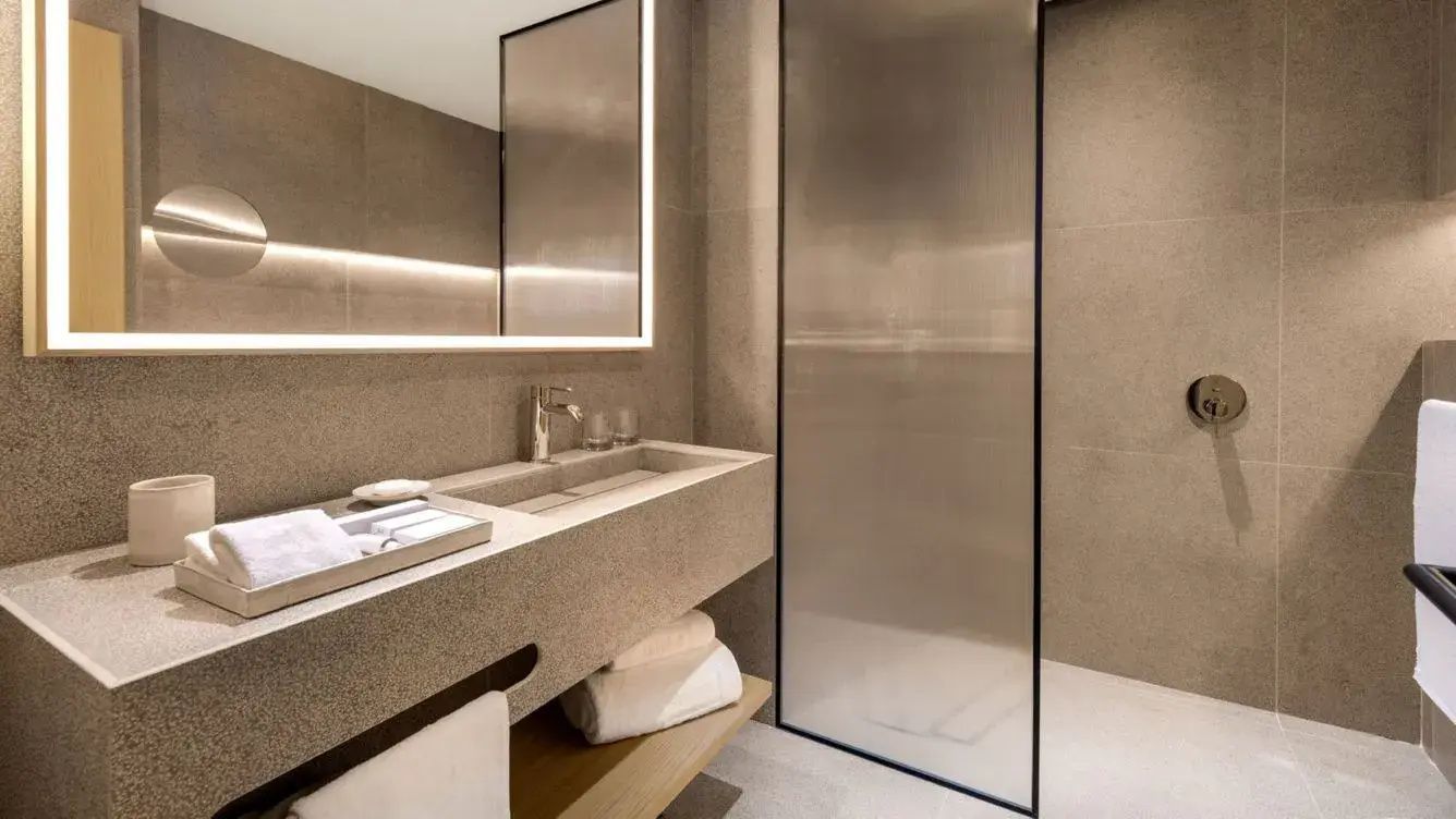 Modernes Badezimmer mit einem Steinwaschbecken, beleuchtetem Spiegel und gläserner Duschkabine.