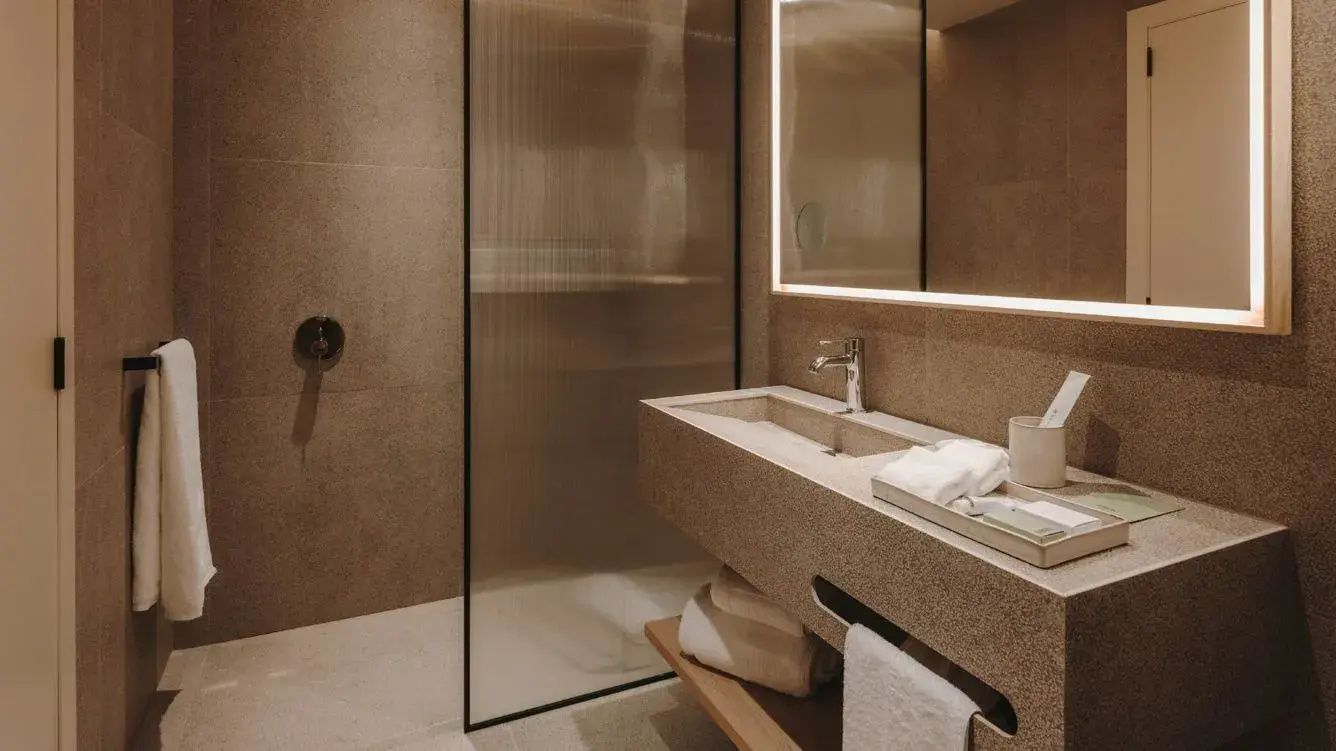 Modernes Badezimmer mit Waschtisch aus Naturstein und beleuchtetem Spiegel.