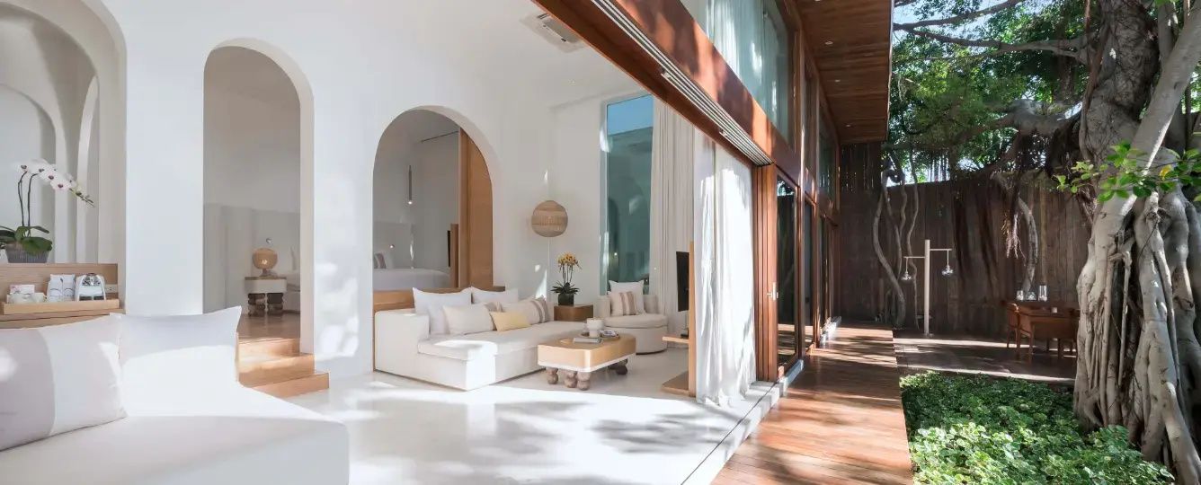 Helles Wohnzimmer in weißem Design mit Sofa, Holztisch, großem Rundbogen und bodentiefen Fenstern.