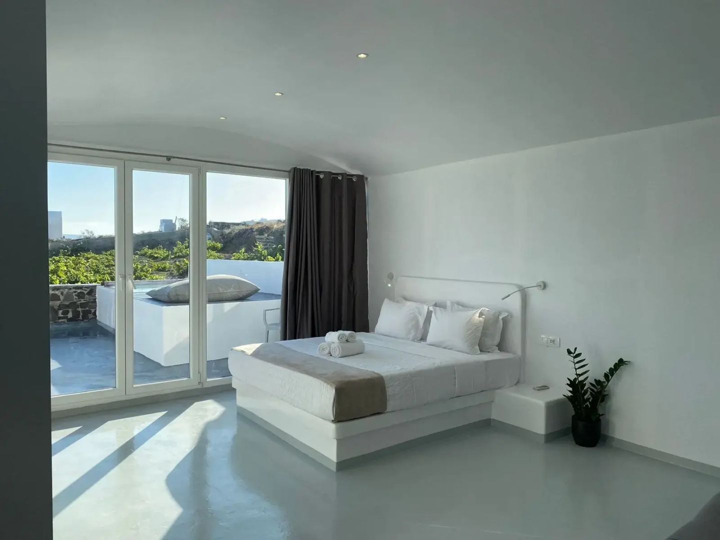 Helles Schlafzimmer mit weißem Doppelbett, Handtüchern und großer Glasfront zur Terrasse.