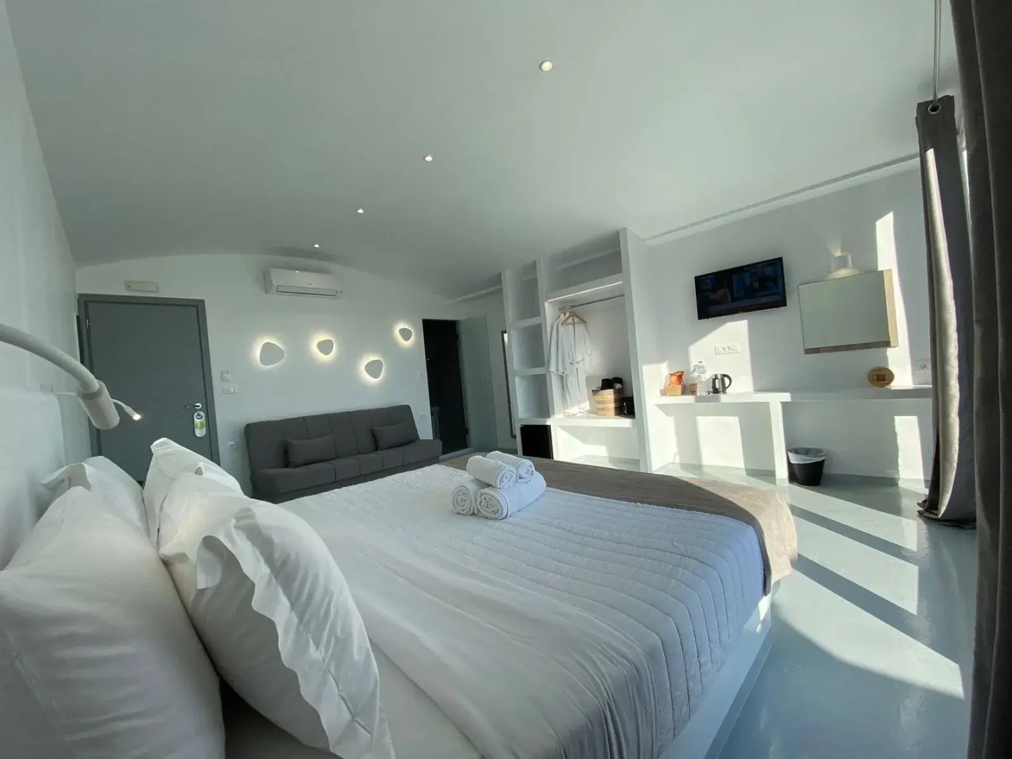 Blick im Zimmer auf graues Sofa, Fernseher an der Wand und verputzte Regale.