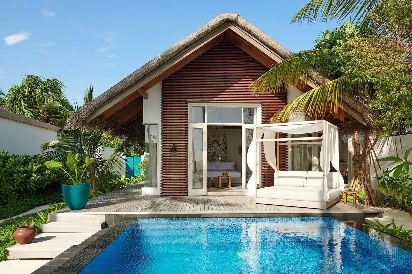 Strandvilla aus Holz mit Reetdach, privatem Pool und einer Tagesliege.