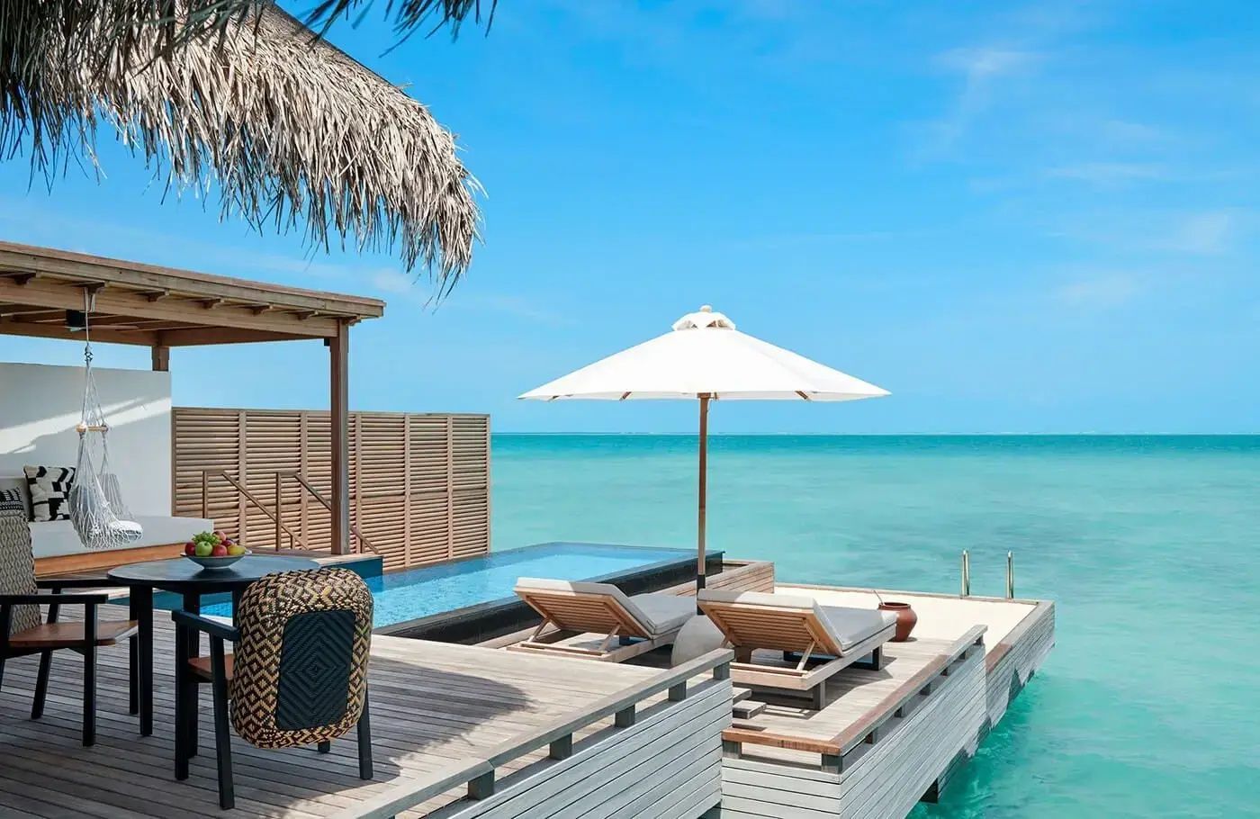 Sonnendeck einer Überwasservilla mit eigenem Pool, Sonnenliegen und Sonnenschirm über dem Meer