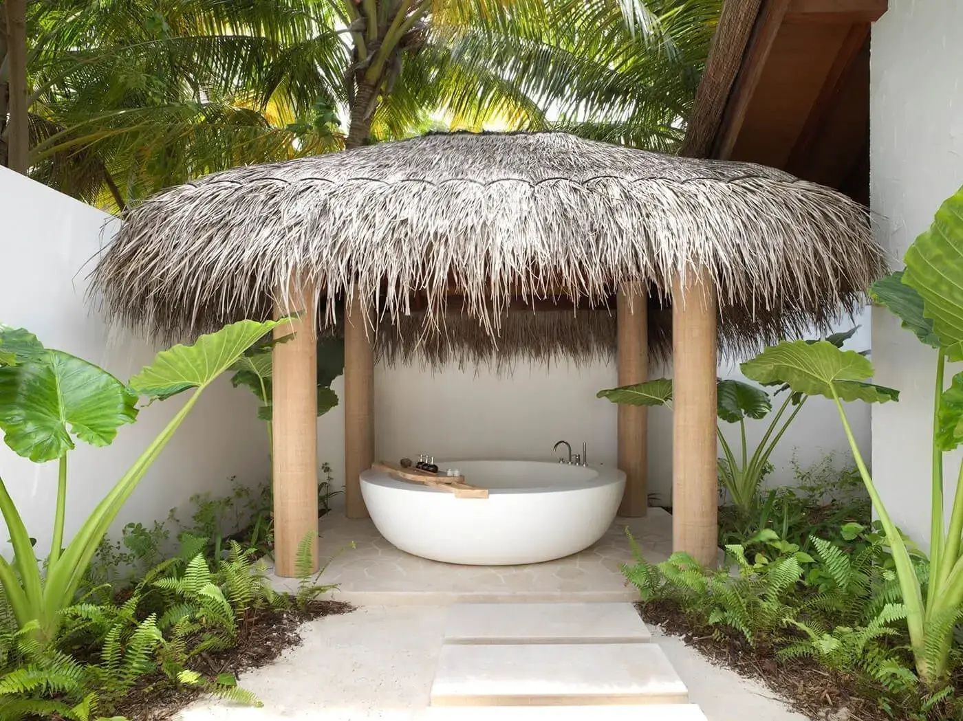 Freistehende runde Badewanne unter einem reetgedeckten Pavillon im grünen Außenbereich.