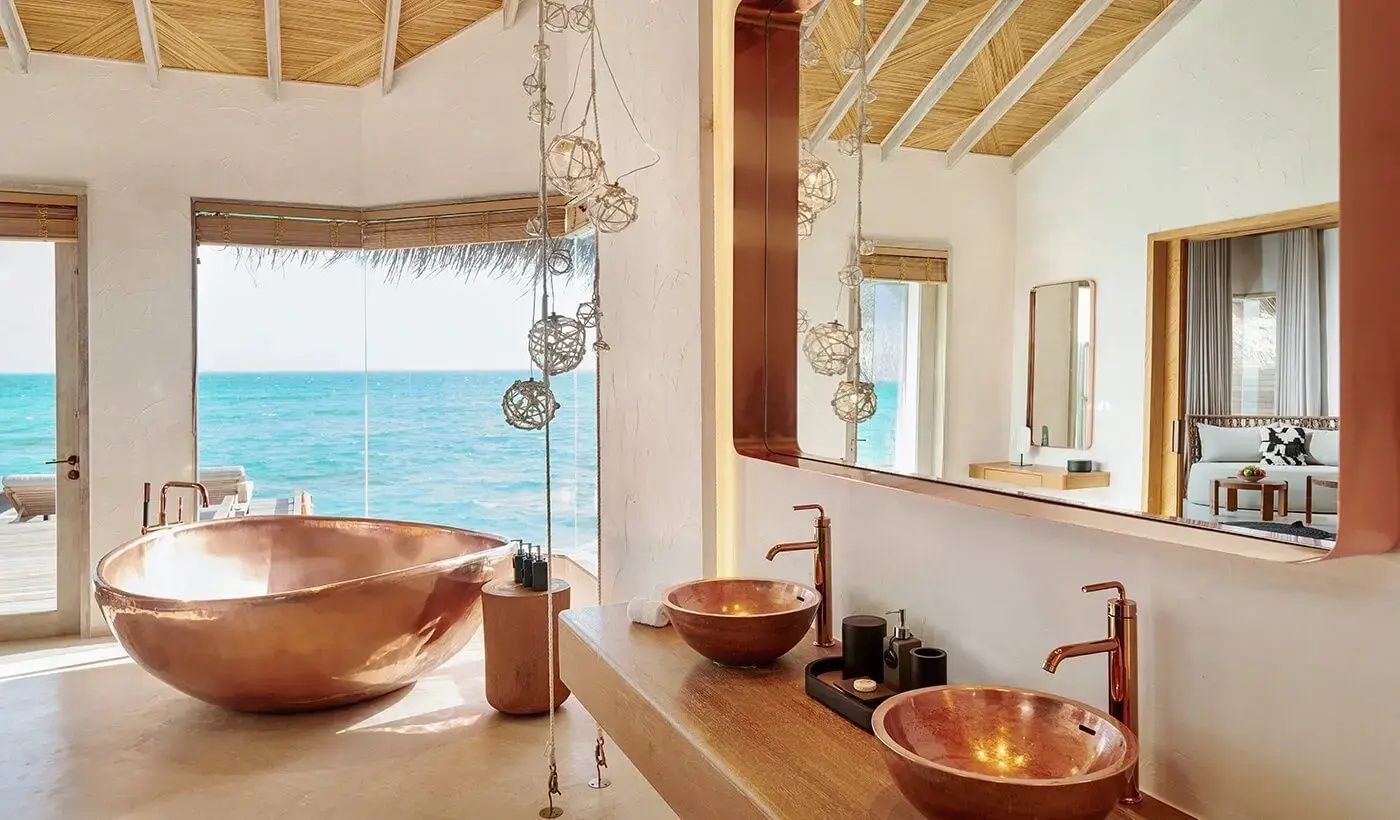 Badezimmer einer Wasservilla mit freistehender Badewanne und Blick auf das Meer