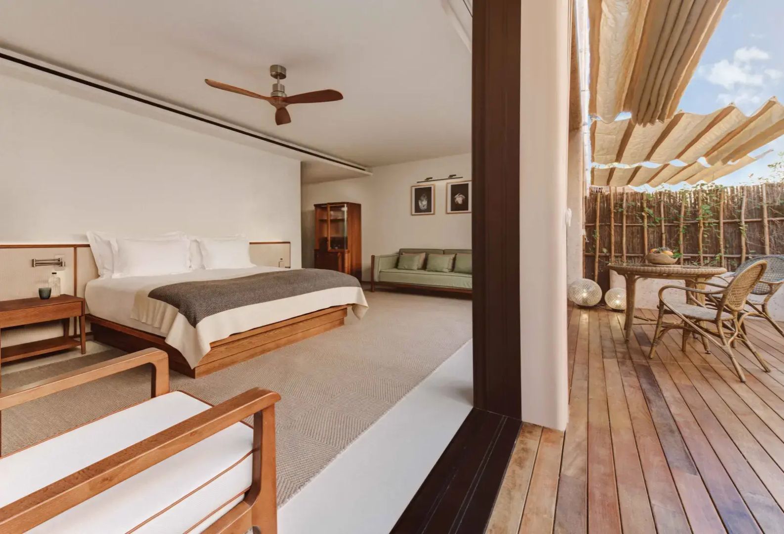 Helles Schlafzimmer mit Holzdoppelbett, Deckenventilator, grünem Sofa und Zugang zur Terrasse.