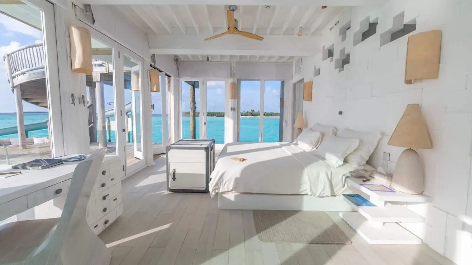 Helles Schlafzimmer mit Doppelbett und Verglasung mit Blick auf das meeresblaue Wasser.
