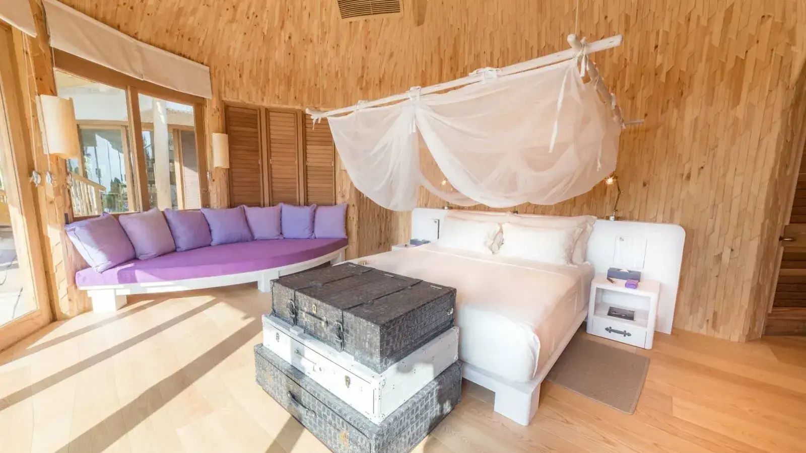 Doppelbett mit Mückennetz und Kisten am Fußende in einem Holzschlafzimmer.