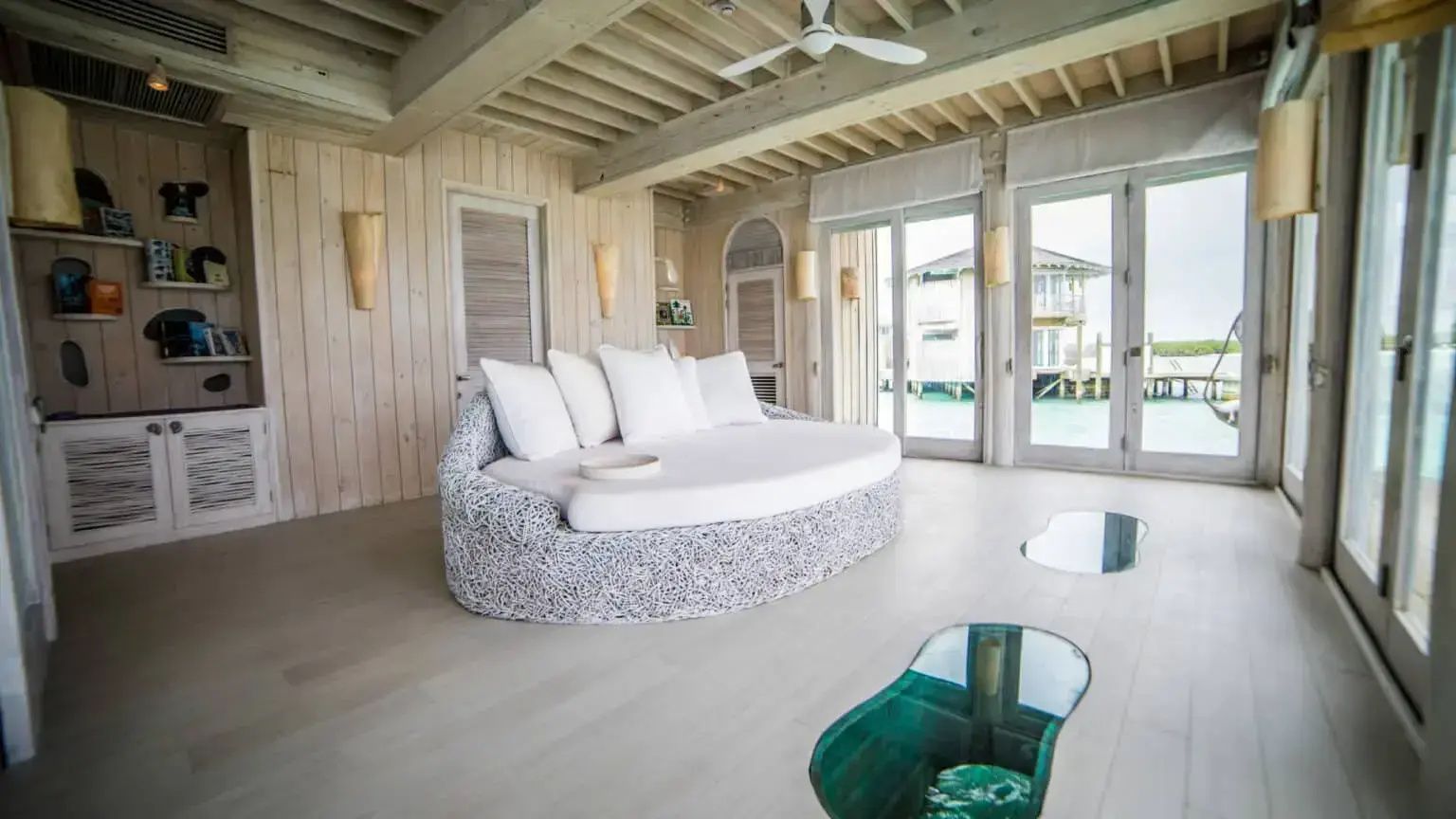 Wohnbereich mit einem runden Sofa, Bodenfenstern zum Meer und Glasflügeltüren.