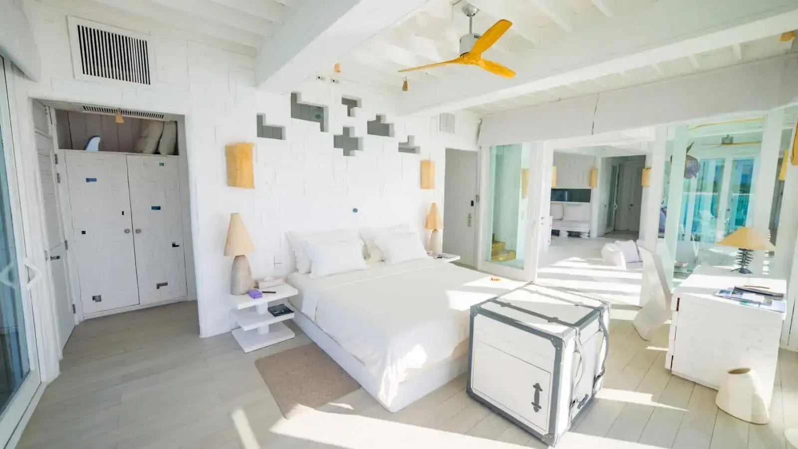 Weißes Schlafzimmer mit Kistentisch am Bettende und gelbem Deckenventilator.