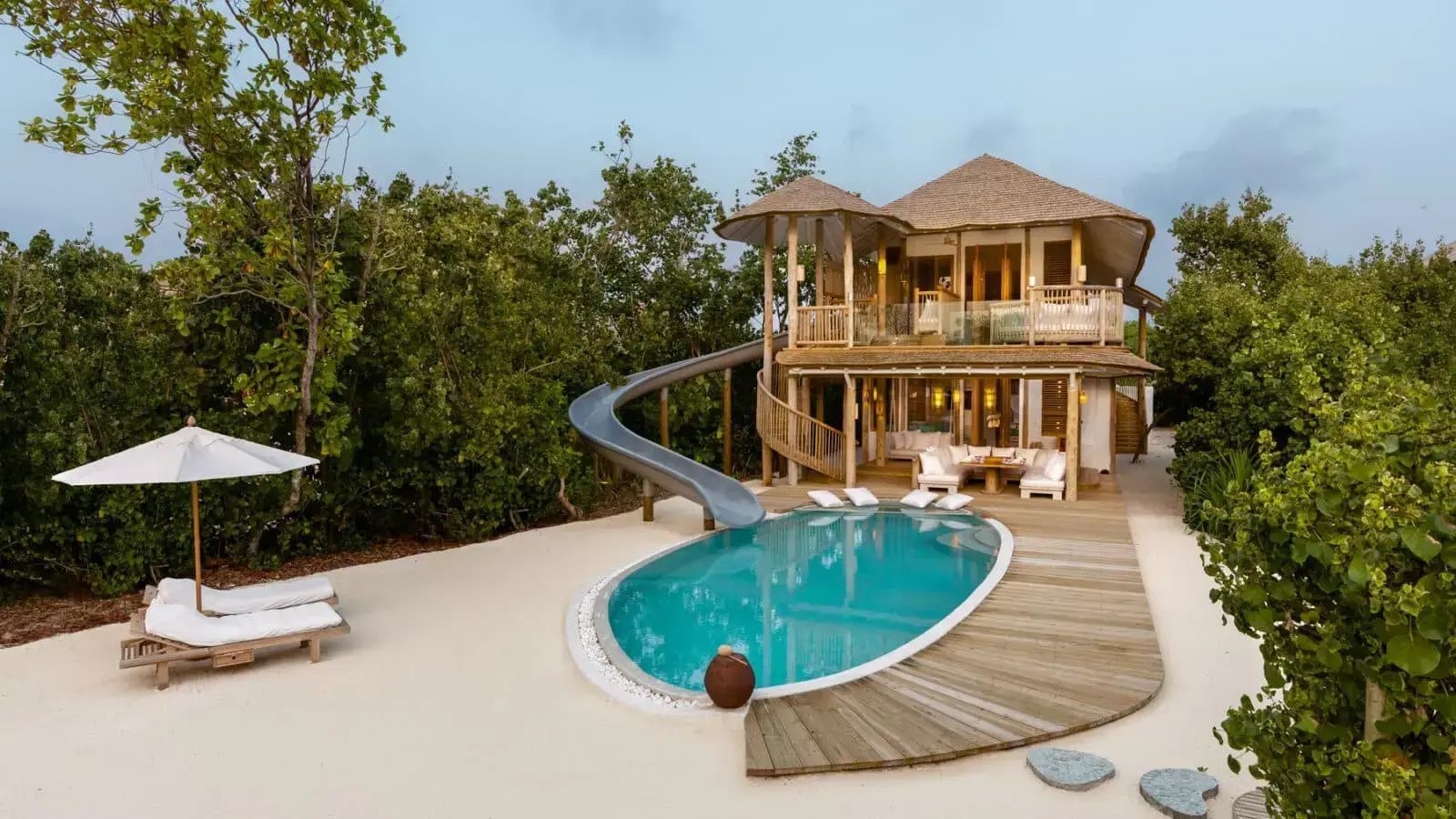 Zweigeschossige Holzvilla mit Reetdach, eigenem Pool und einer Wasserrutsche ins Wasser.