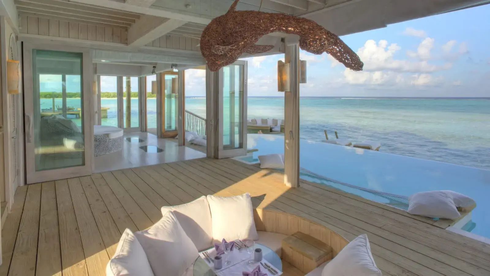 Holzterrasse mit Sitzecke, Infinitypool und Weitblick auf das türkisfarbene Meer.