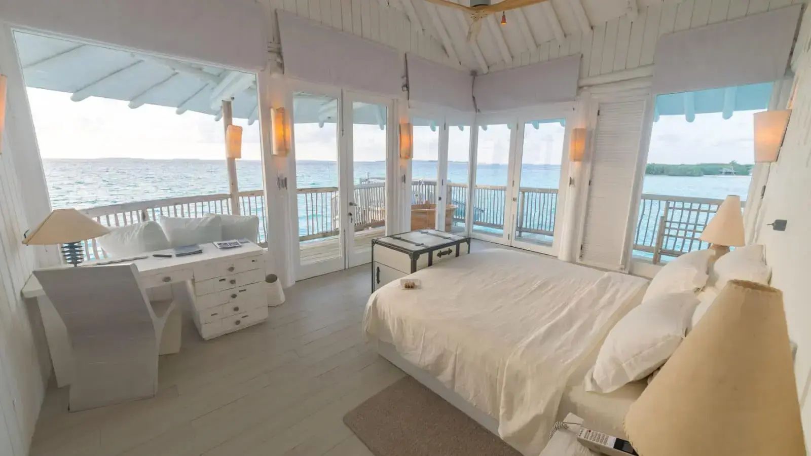 Heller Schlafraum in einer Überwasservilla mit großem Doppelbett und Panoramablick auf das Meer.