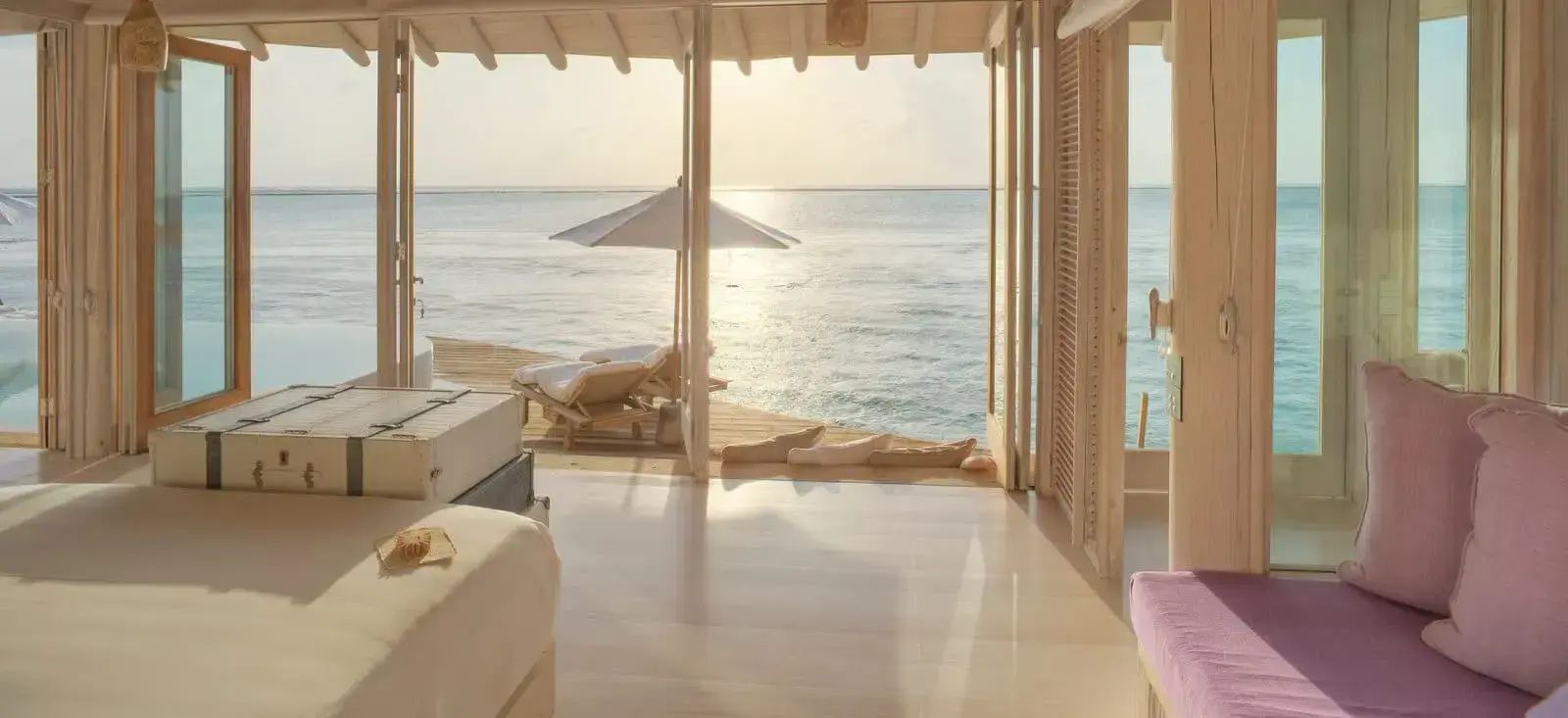 Blick aus der Villa auf eine Sonnenterrasse mit Liegen und Schirm direkt am Ozean.