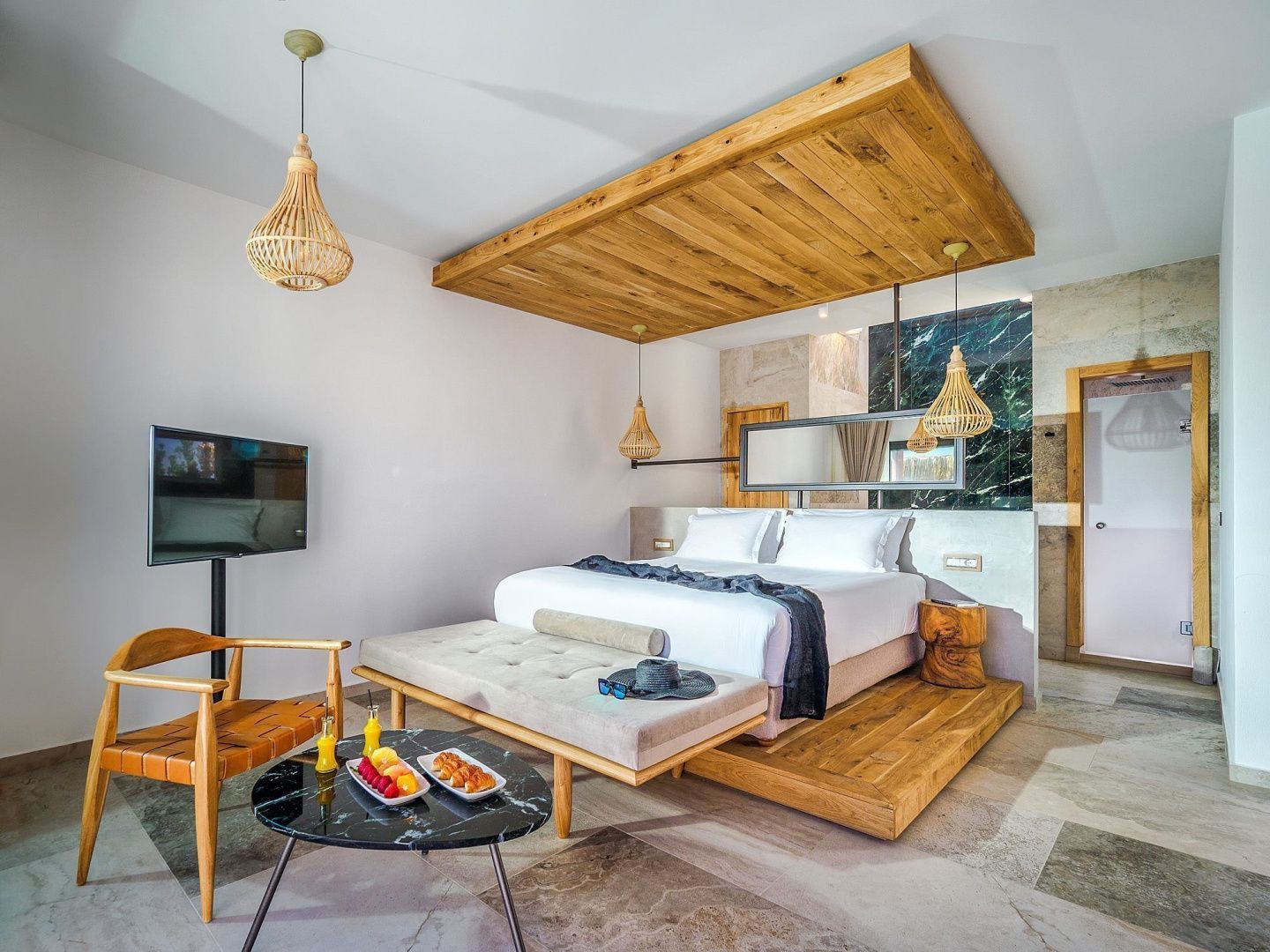 Helles Hotelzimmer mit großem Doppelbett, Holzdecke und Beistelltisch mit Erfrischungen.