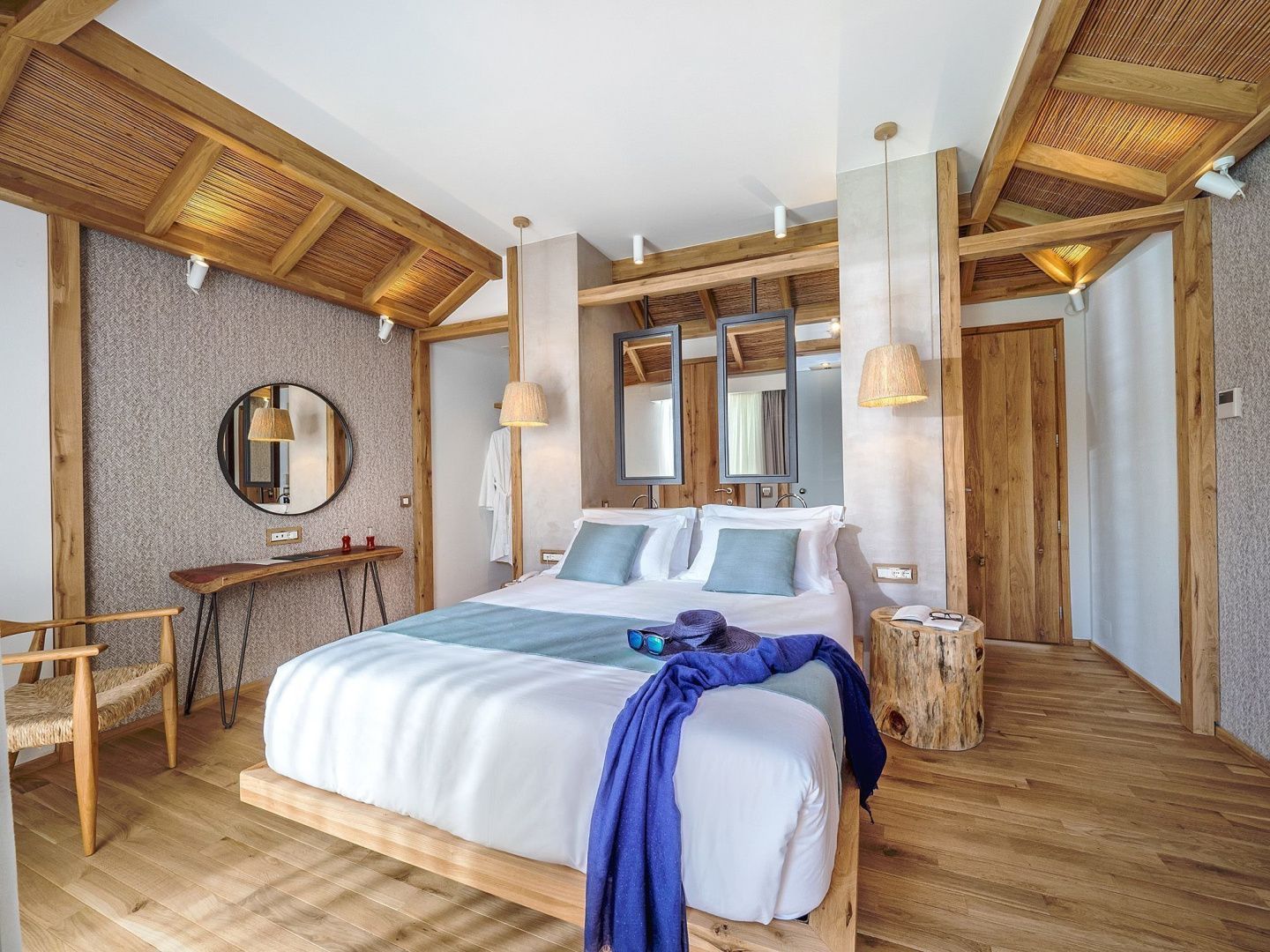 Doppelbett mit hellblauer Tagesdecke in einem hellen Hotelzimmer mit Holzelementen.