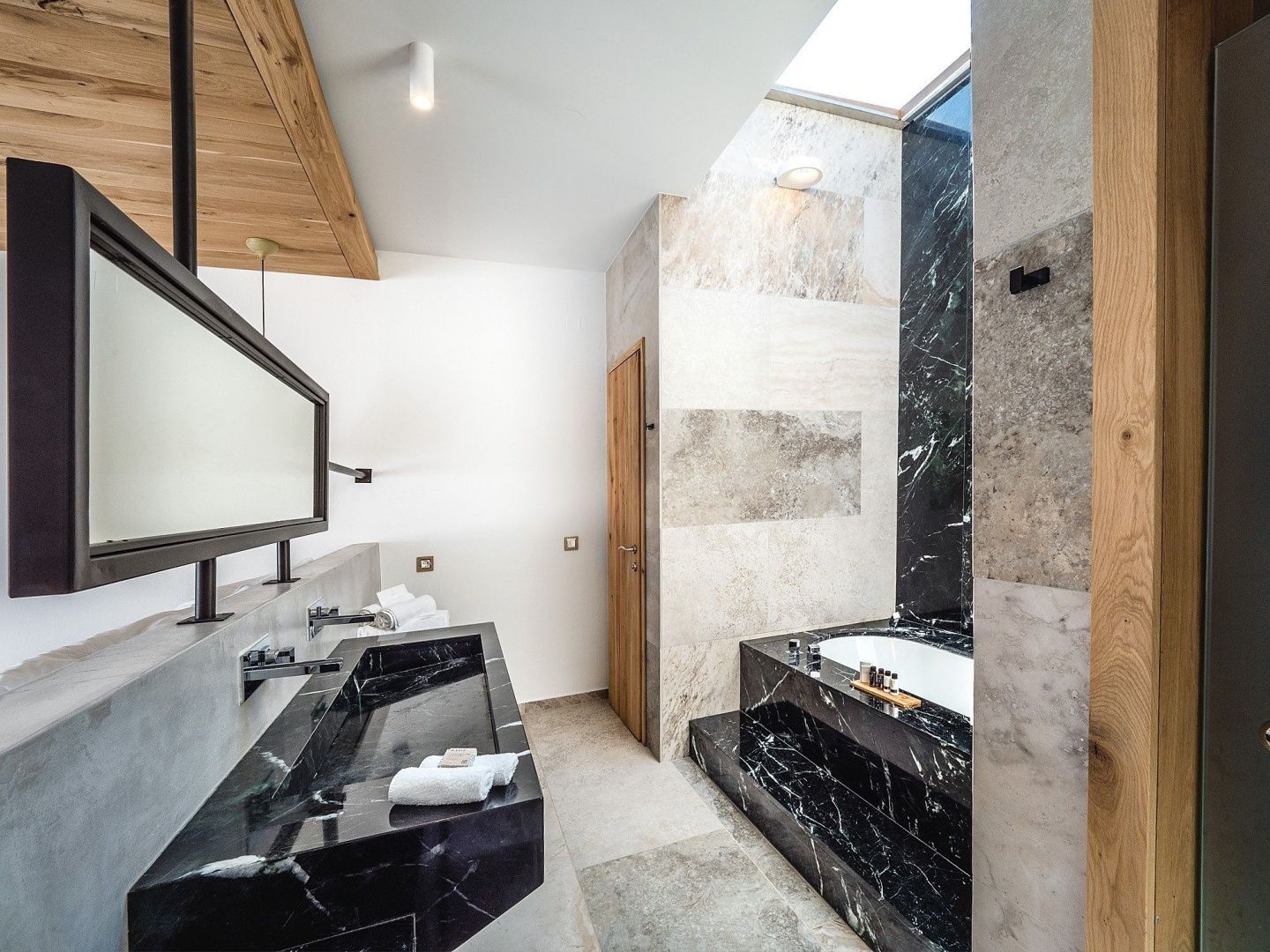 Modernes Badezimmer mit schwarzem Marmorwaschbecken und Badewanne unter einem Dachfenster.