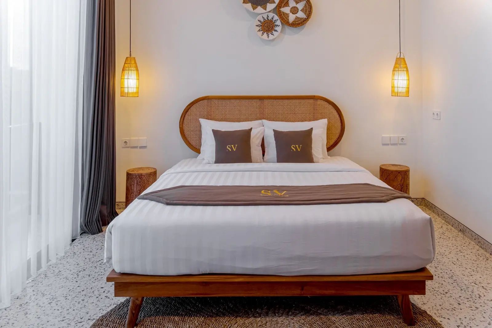 Doppelbett mit weißer Bettwäsche, Kopfteil aus Holz und zwei hängenden Lampen im Zimmer.