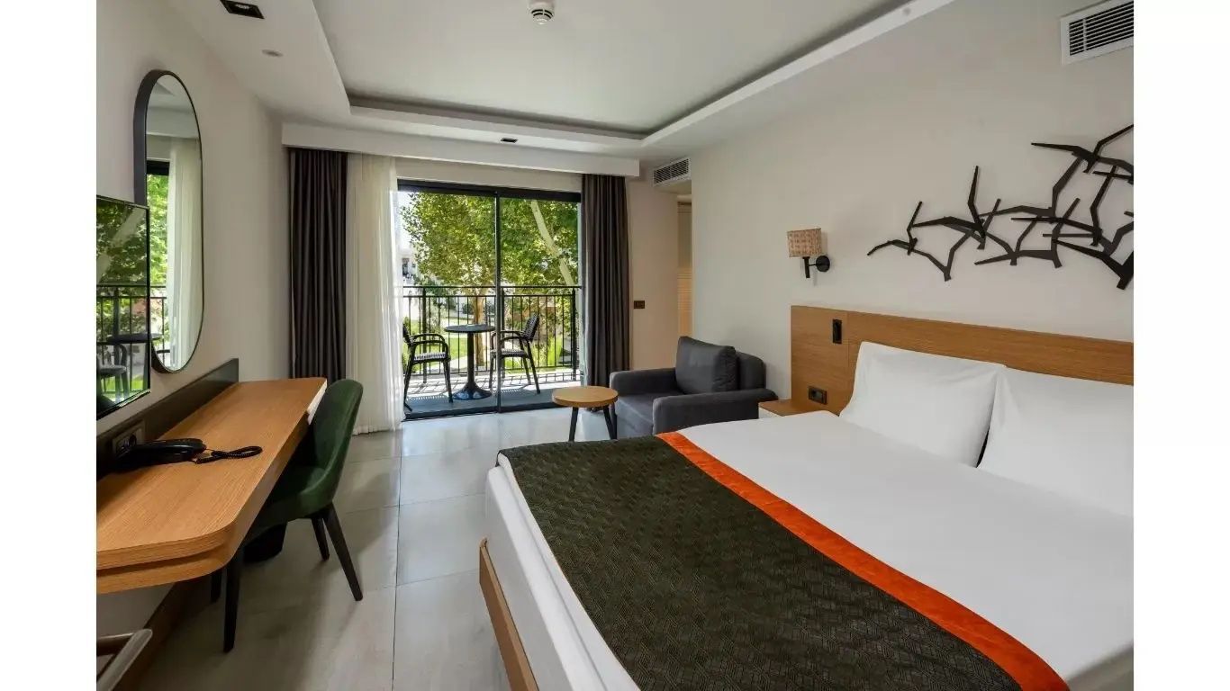 Modernes Hotelzimmer mit Doppelbett, Sessel und Balkon mit Blick ins Grüne.