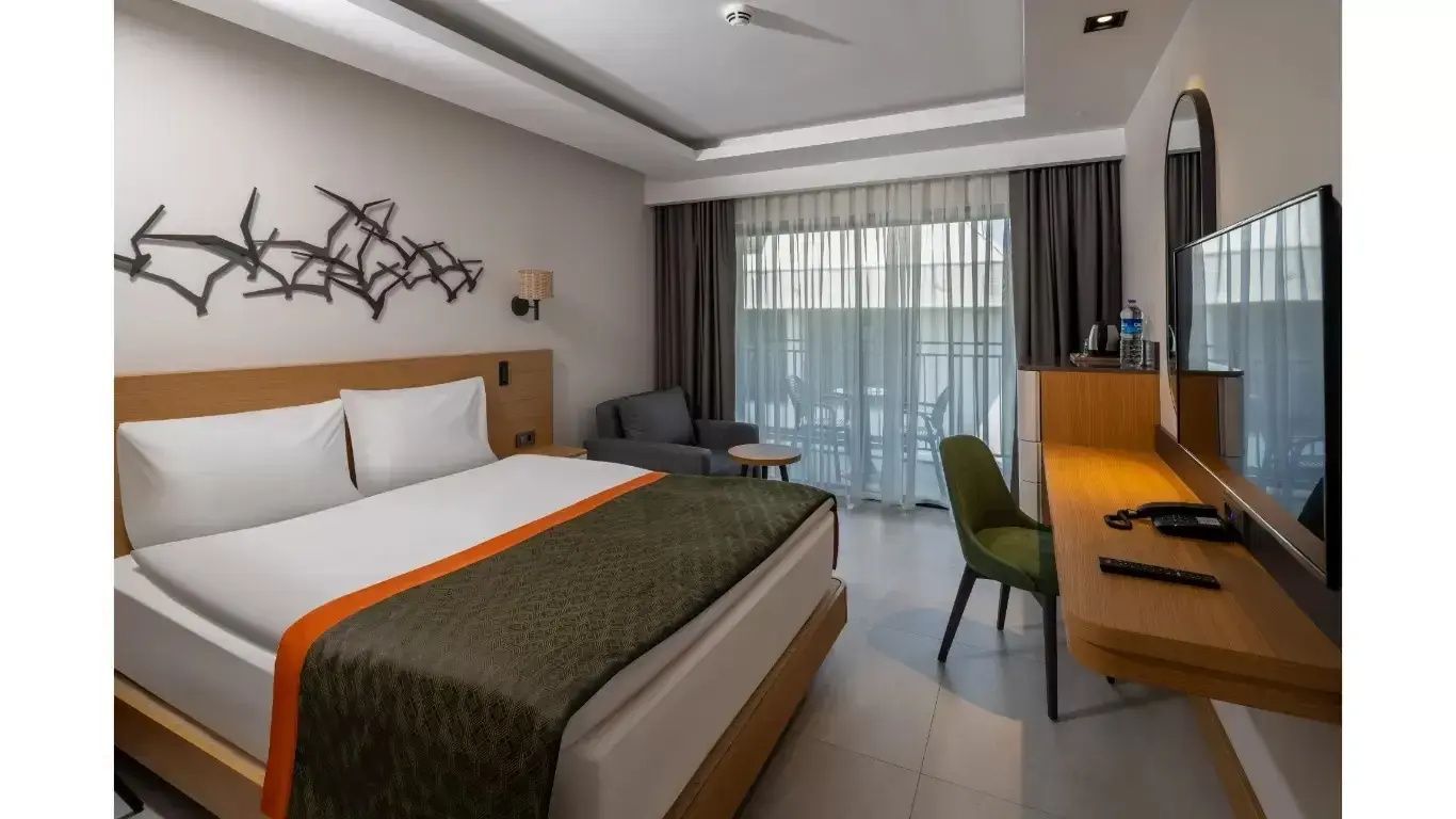 Modernes Hotelzimmer mit Doppelbett, Sessel, Schreibtisch und Zugang zum Balkon.