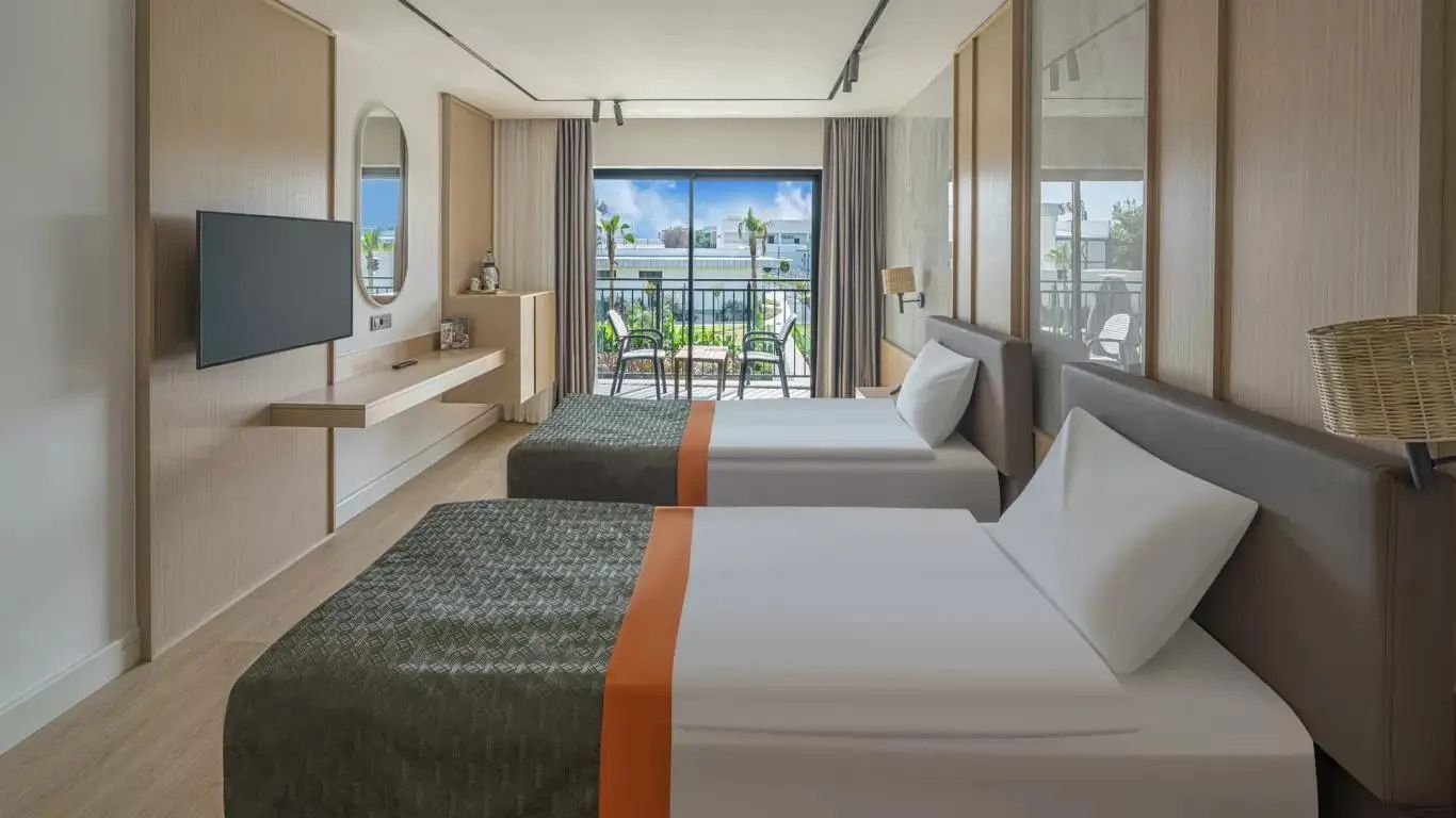 Helles Hotelzimmer mit zwei Einzelbetten, Schreibtisch und Balkon mit Blick ins Grüne.