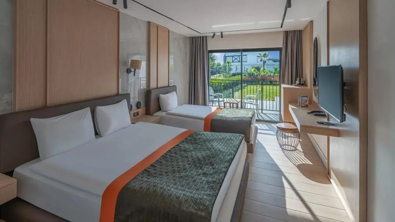 Helles Hotelzimmer mit zwei Betten, Blick durch die Balkontür auf den Garten.